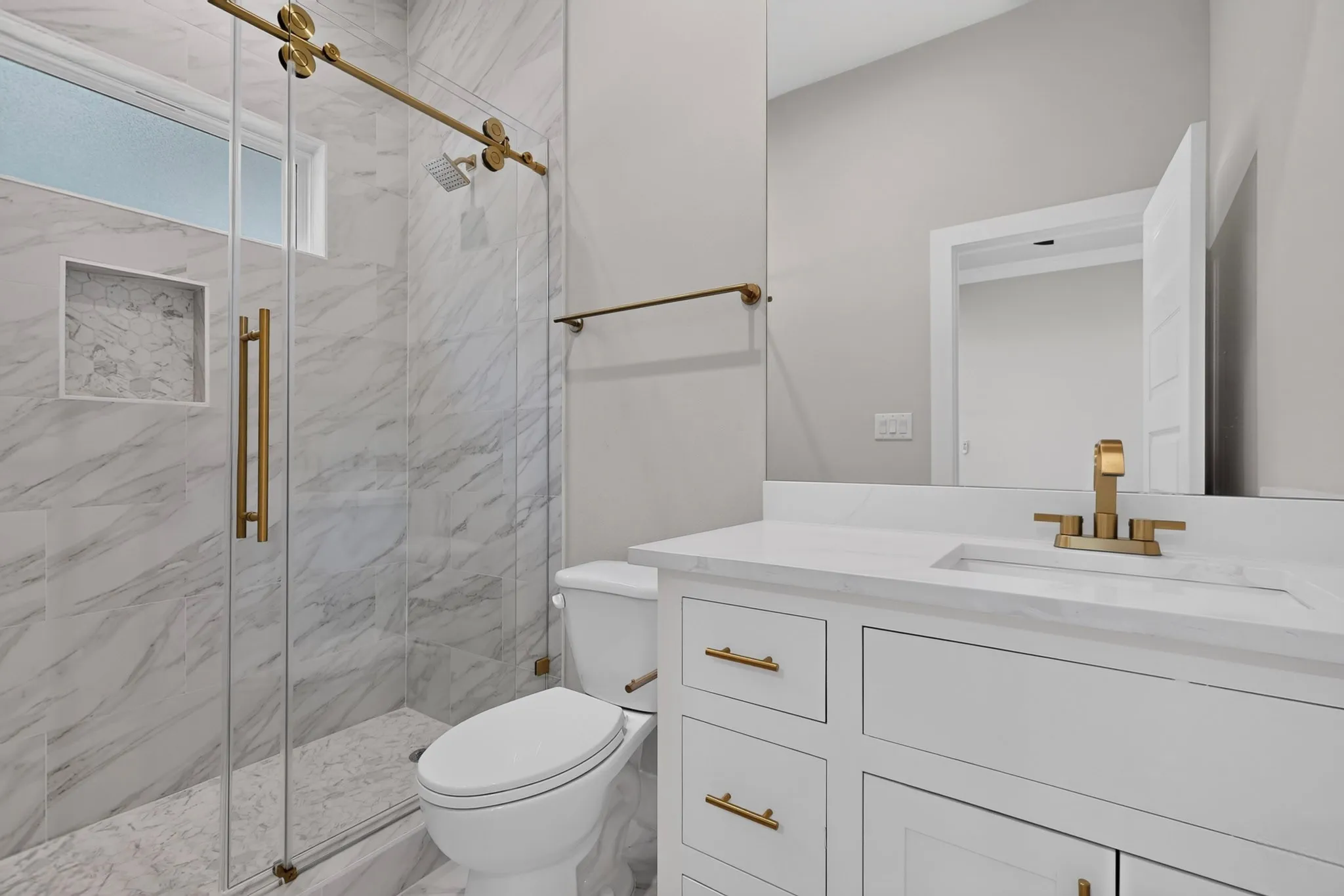Glass-enclosed shower with a gold-tone sliding door mechanism and a built-in niche