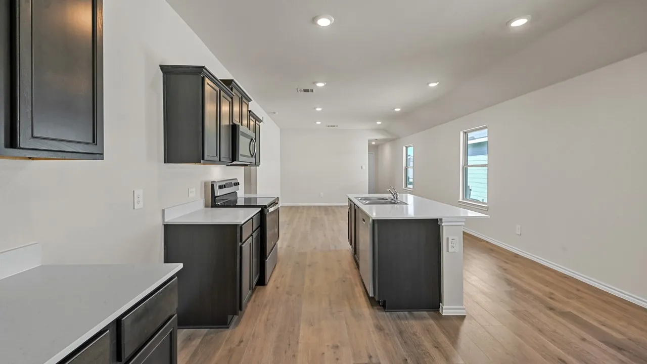 Kitchen featuring dark wood cabinetry, light-toned countertops, stainless steel appliances, and a central island with an undermount sink