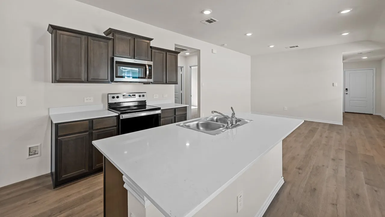 Kitchen featuring wood-finish cabinetry, stainless steel appliances, a center island with an integrated sink, and white countertops