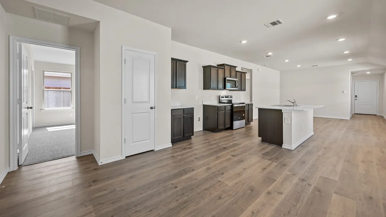Open-concept living area featuring wood-finish flooring, recessed lighting, and a kitchen with dark cabinetry and a center island with a sink