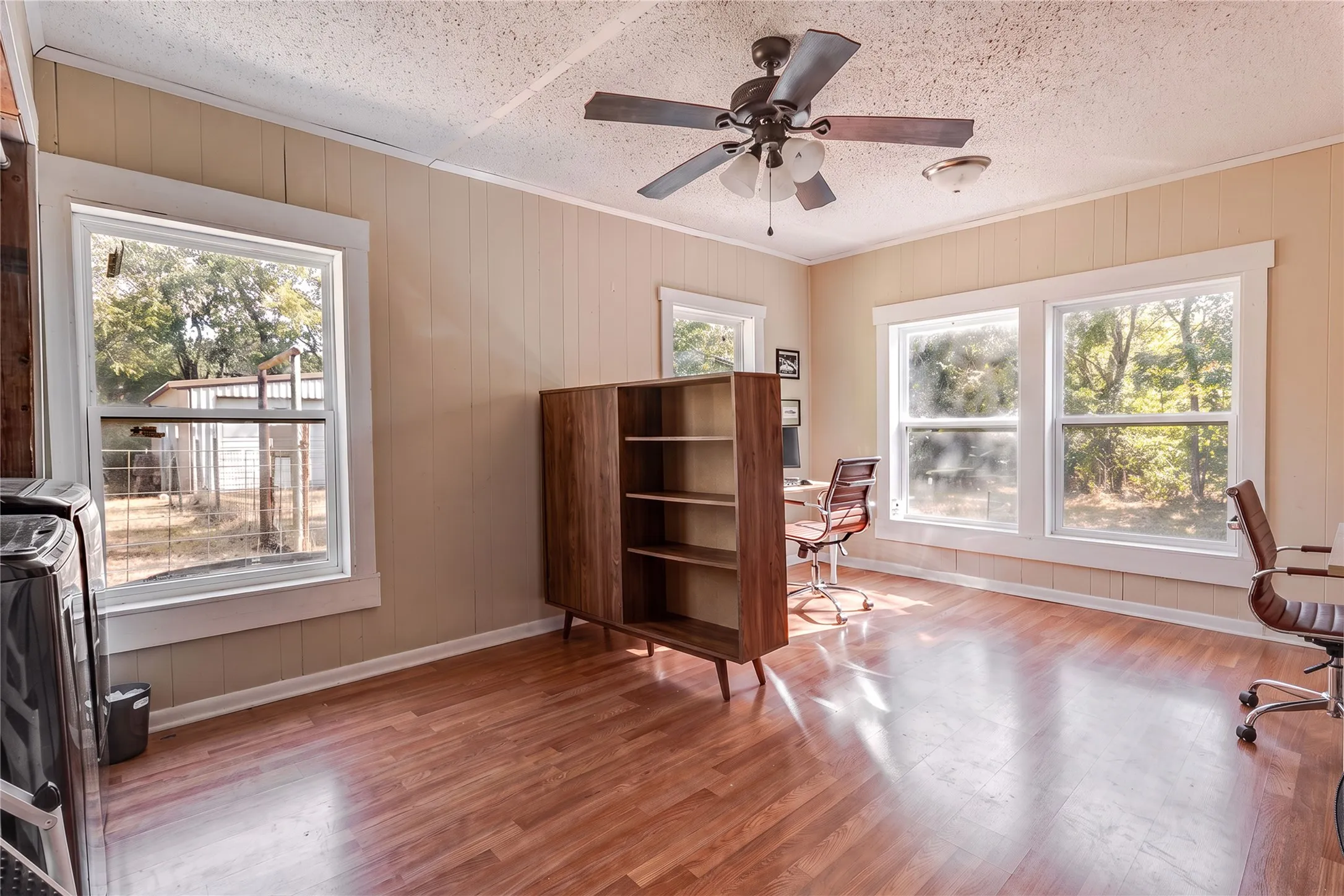 Wood-finish flooring, multiple windows, ceiling fan, and painted paneling