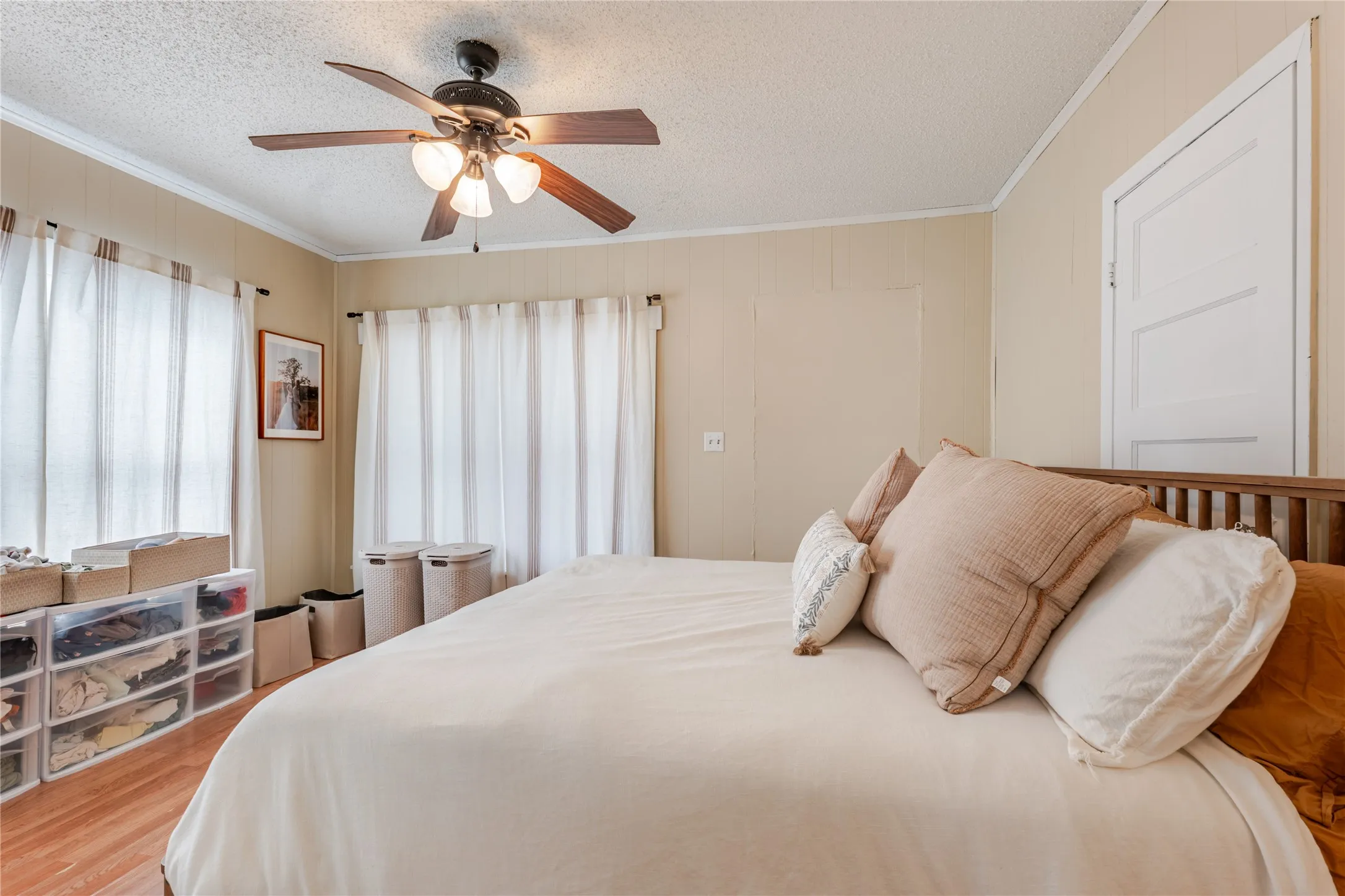 Wood-finish flooring, multiple windows with natural light, ceiling fan with integrated lighting, and a paneled door