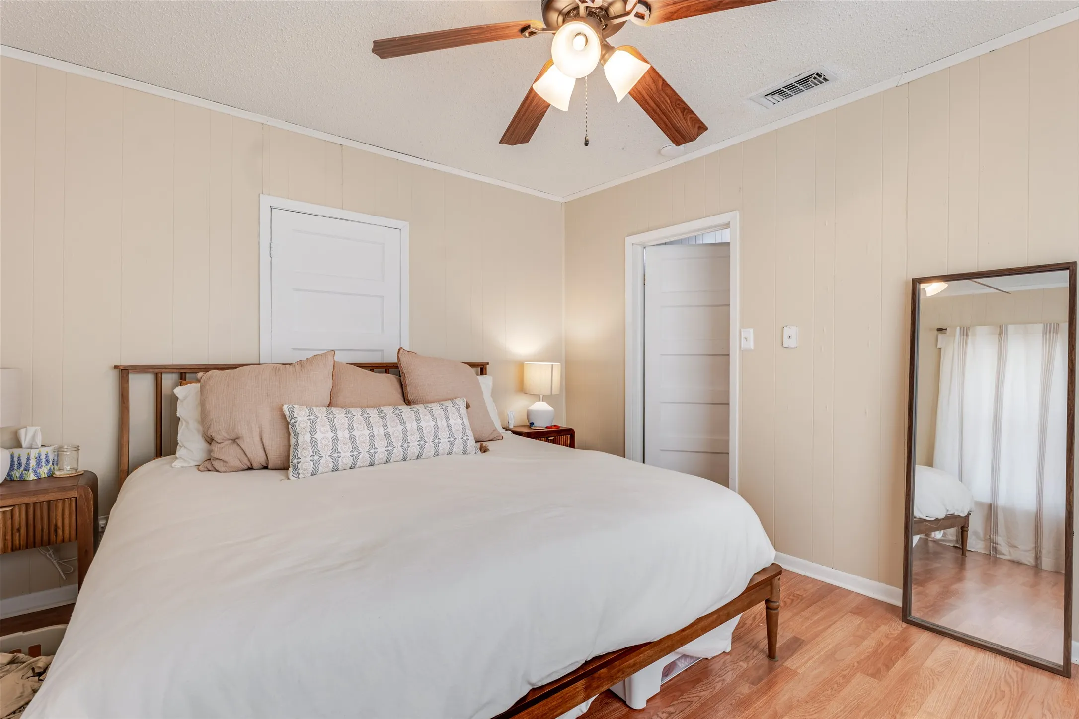 Wood-finish flooring with neutral wall paneling, ceiling fan with integrated lighting, and white trim