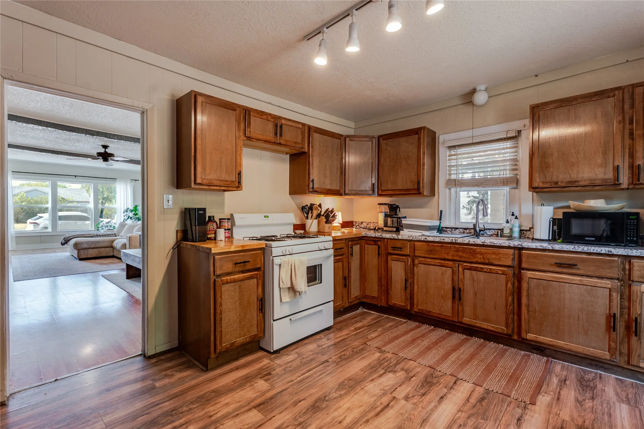 Wood-finish flooring, wood cabinetry, track lighting, and a built-in oven