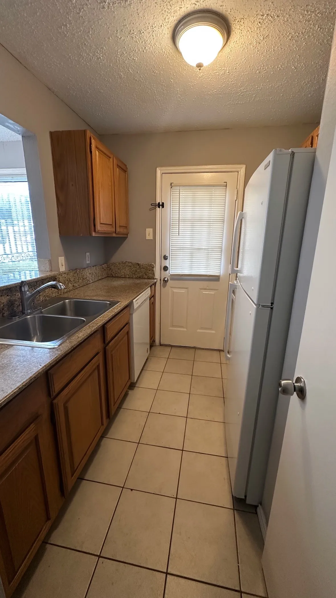 Kitchen featuring wood-finish cabinetry, granite-style countertops, stainless steel double basin sink, and tile flooring