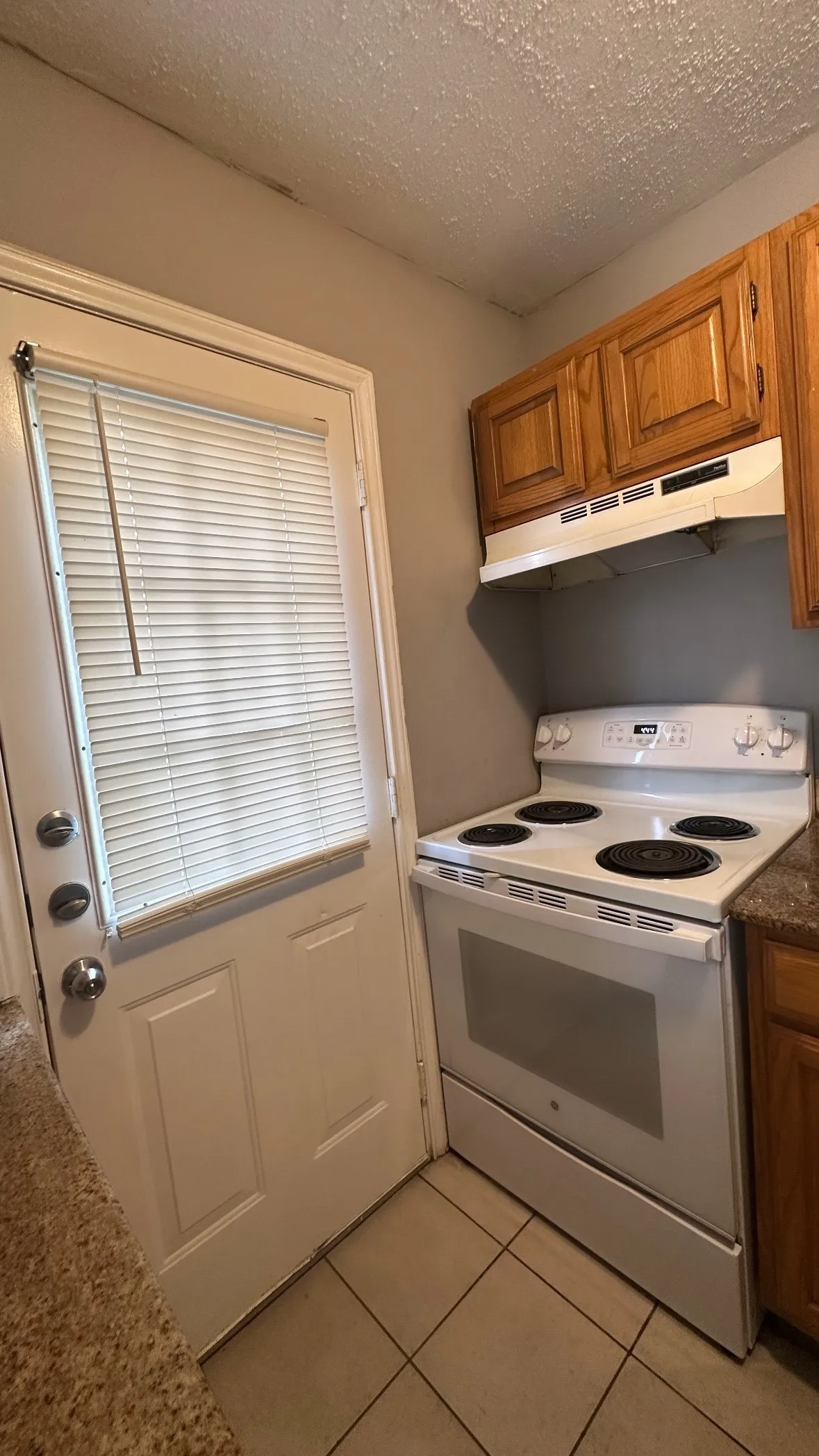 White electric range, wood cabinetry, and tile flooring