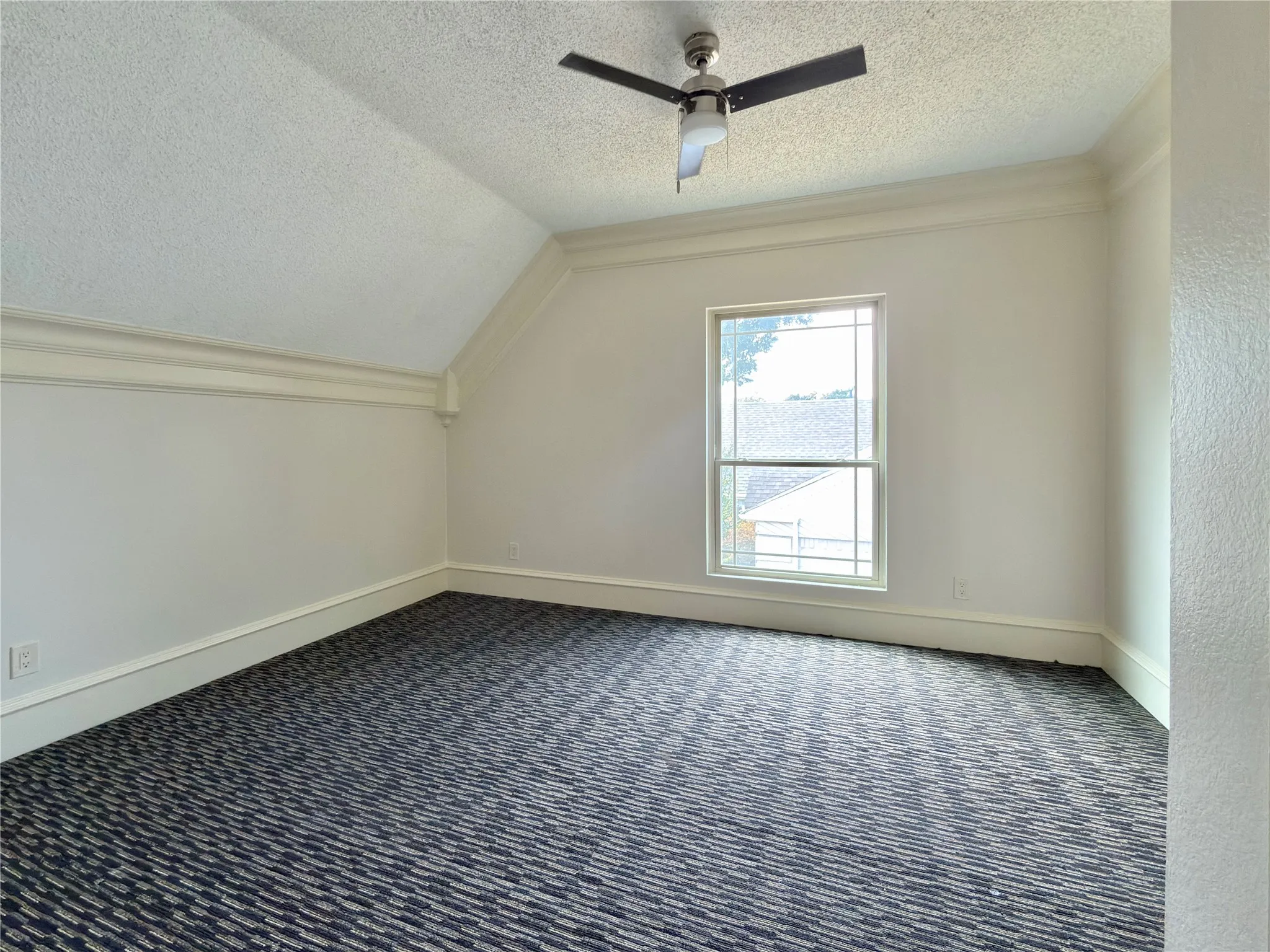 Sloped ceiling with crown molding, window with grid panes, ceiling fan, and patterned carpet