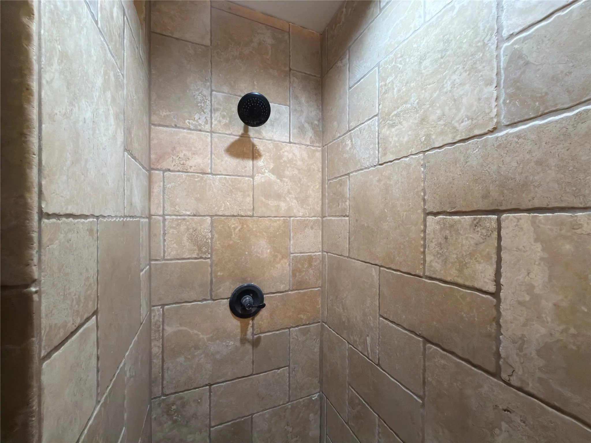 Shower enclosure with natural stone-look tile, dark bronze-finish shower head, and dark bronze-finish shower controls