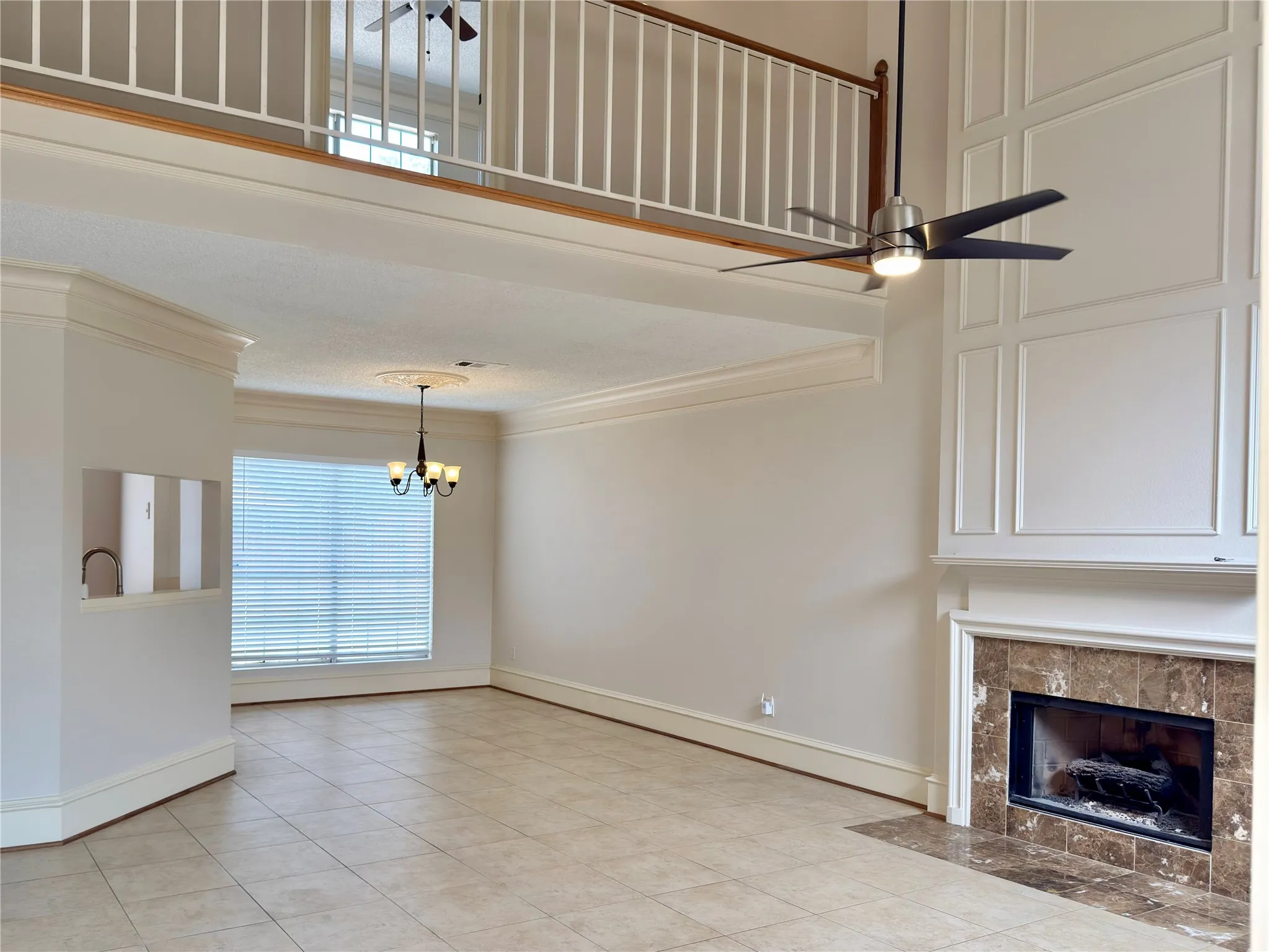 Two-story living area featuring a fireplace with a stone surround, decorative wall paneling, and a loft overlook