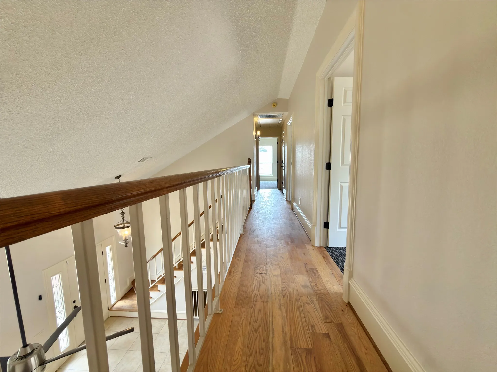 Wood-finish flooring throughout the hallway, white painted walls, and a white railing with a wood-finish handrail