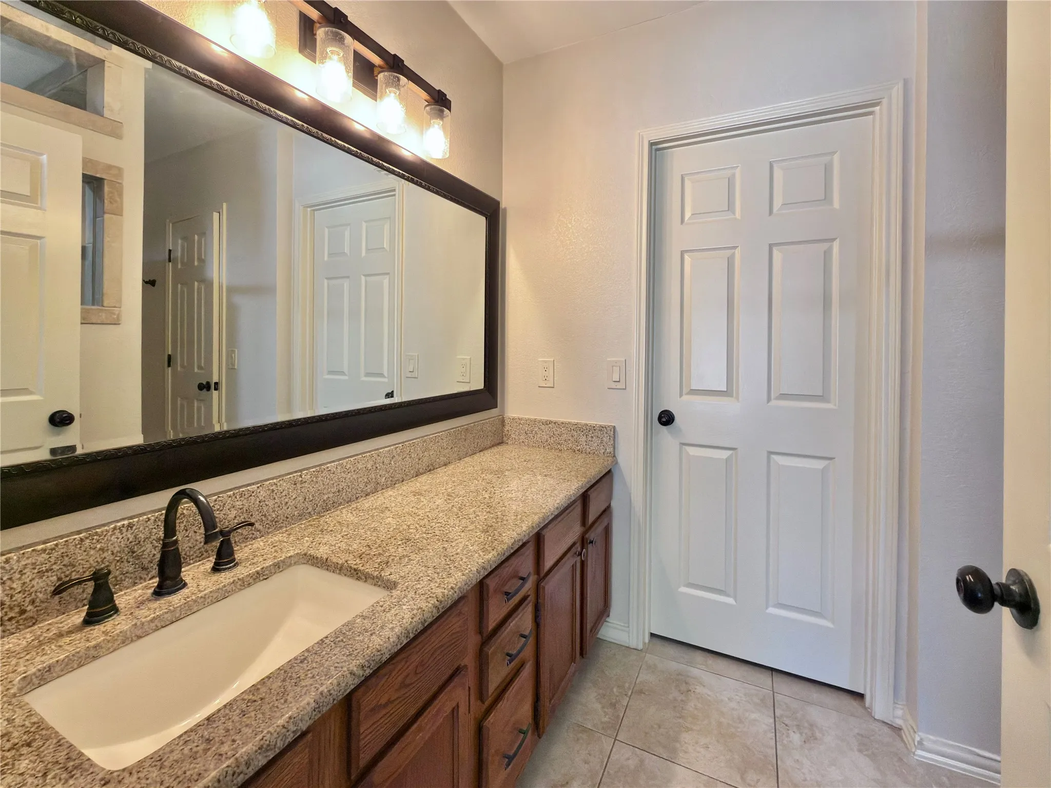 Spacious vanity featuring an integrated sink, dark bronze fixtures, and a granite-style countertop