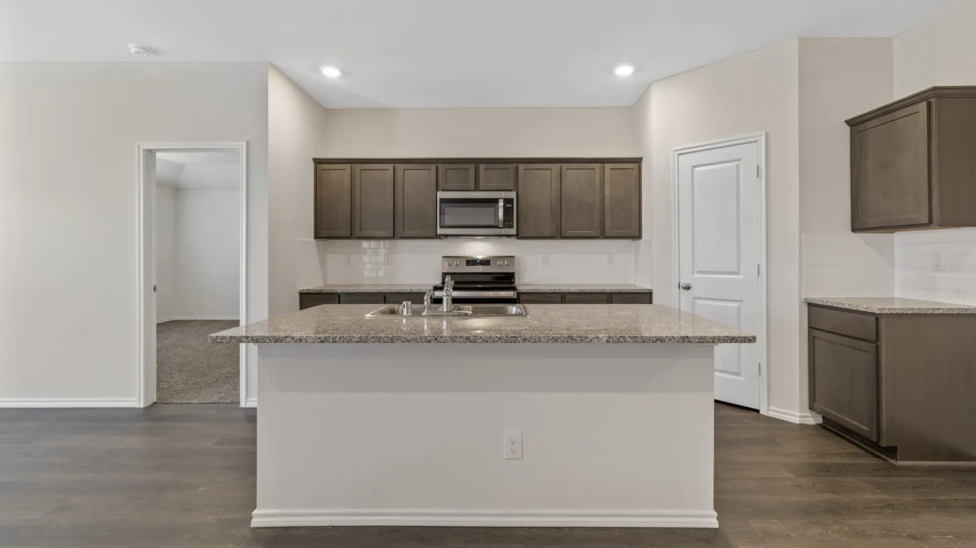 Kitchen featuring an island with a built-in sink, stainless steel appliances, dark wood-finish cabinetry, and a white subway tile backsplash