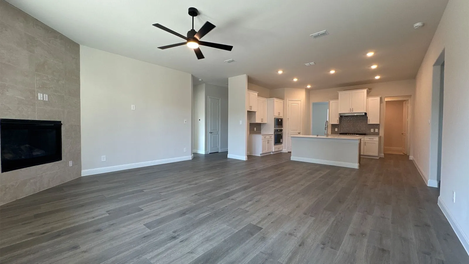Spacious open-concept interior featuring wood-finish flooring, a contemporary fireplace with tile surround, a ceiling fan, recessed lighting, and a kitchen island with a sink and pendant lighting