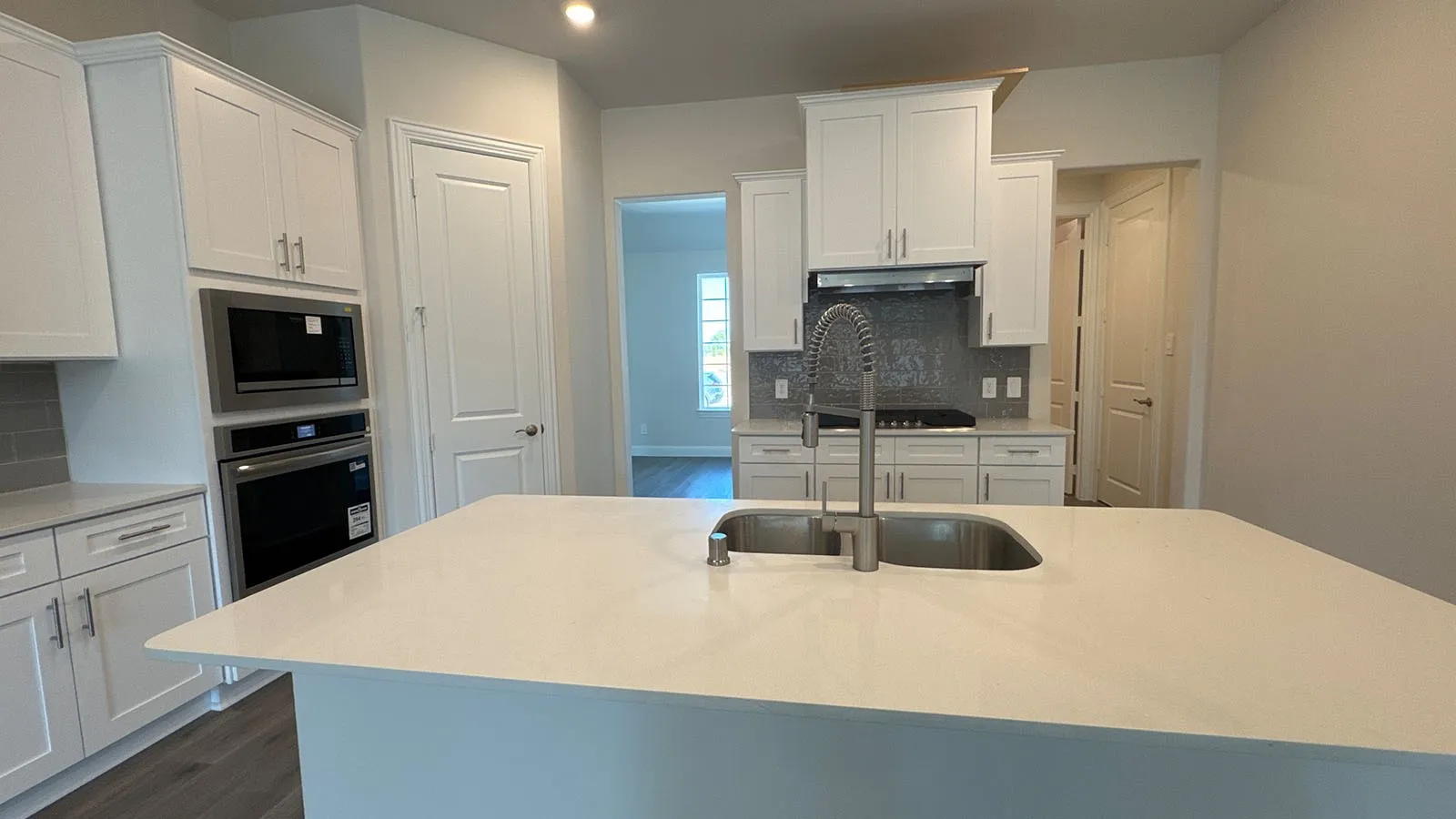 Kitchen featuring white shaker-style cabinetry, stainless steel appliances, a white solid surface island with double basin sink, and a gray subway tile backsplash