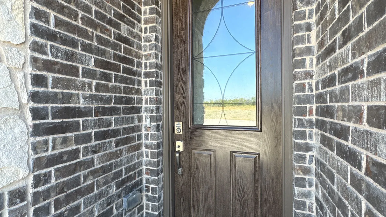 Dark brick exterior with stone accents, a wood-finish entry door, decorative glass insert, and smart lock hardware