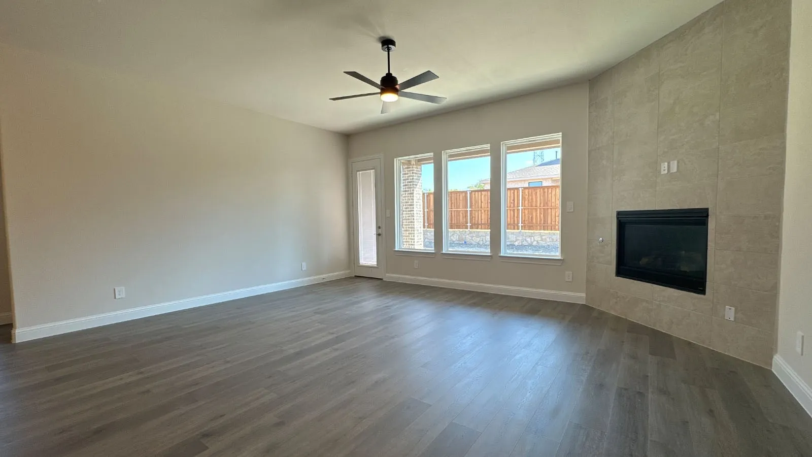 Spacious living area featuring wood-finish flooring, a ceiling fan, a tiled fireplace, and multiple windows