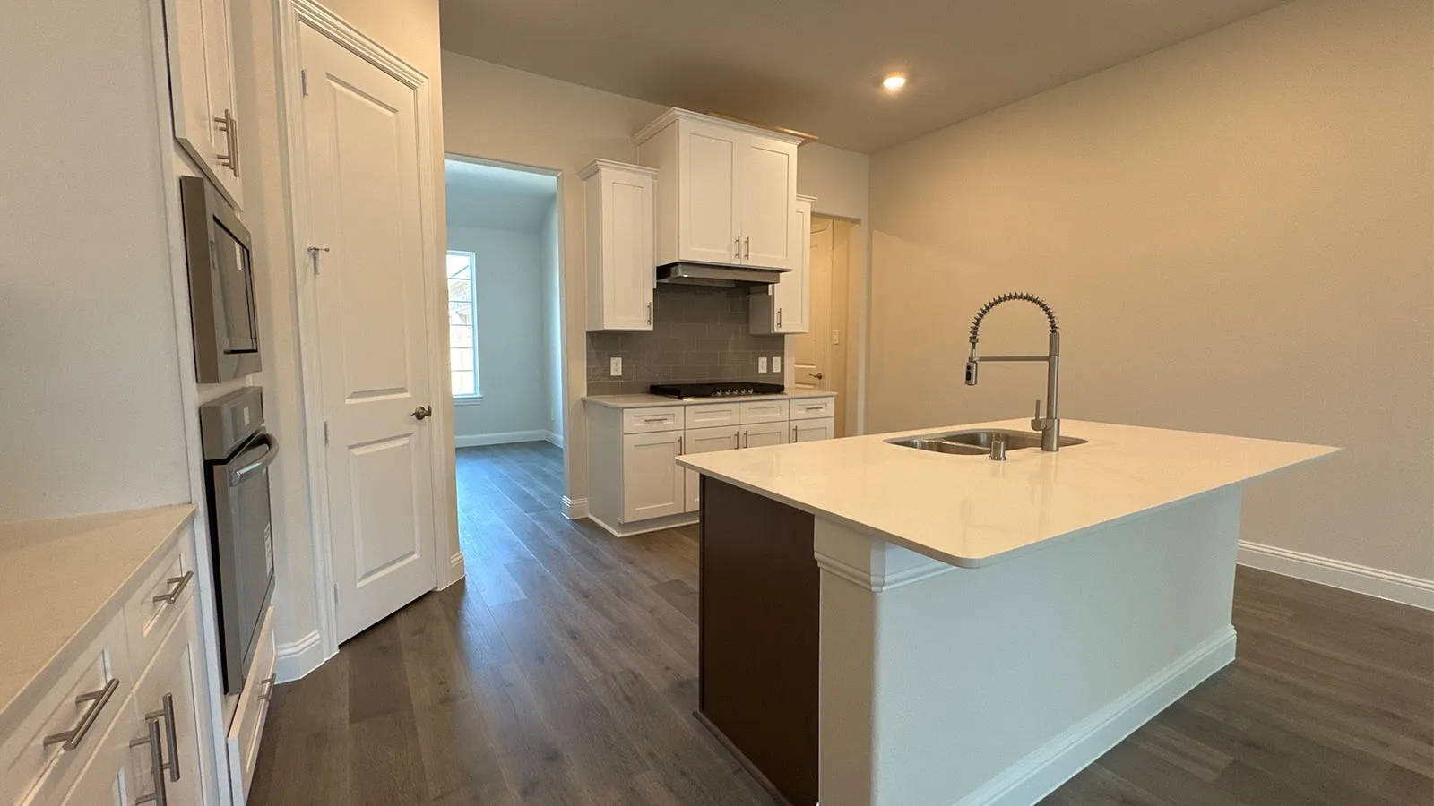 Kitchen featuring a central island with an integrated sink, white cabinetry, wood-finish flooring, and stainless steel built-in ovens