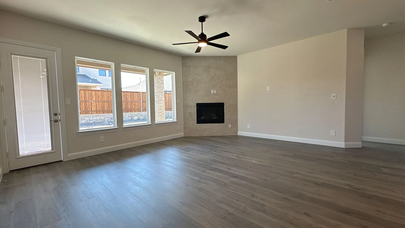 Spacious living area featuring wood-finish flooring, a corner fireplace with tile surround, multiple windows, and a ceiling fan