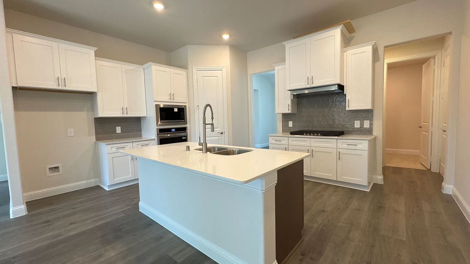 Kitchen featuring a large central island with an integrated sink, built-in stainless steel appliances, white cabinetry, a tile backsplash, and wood-finish flooring