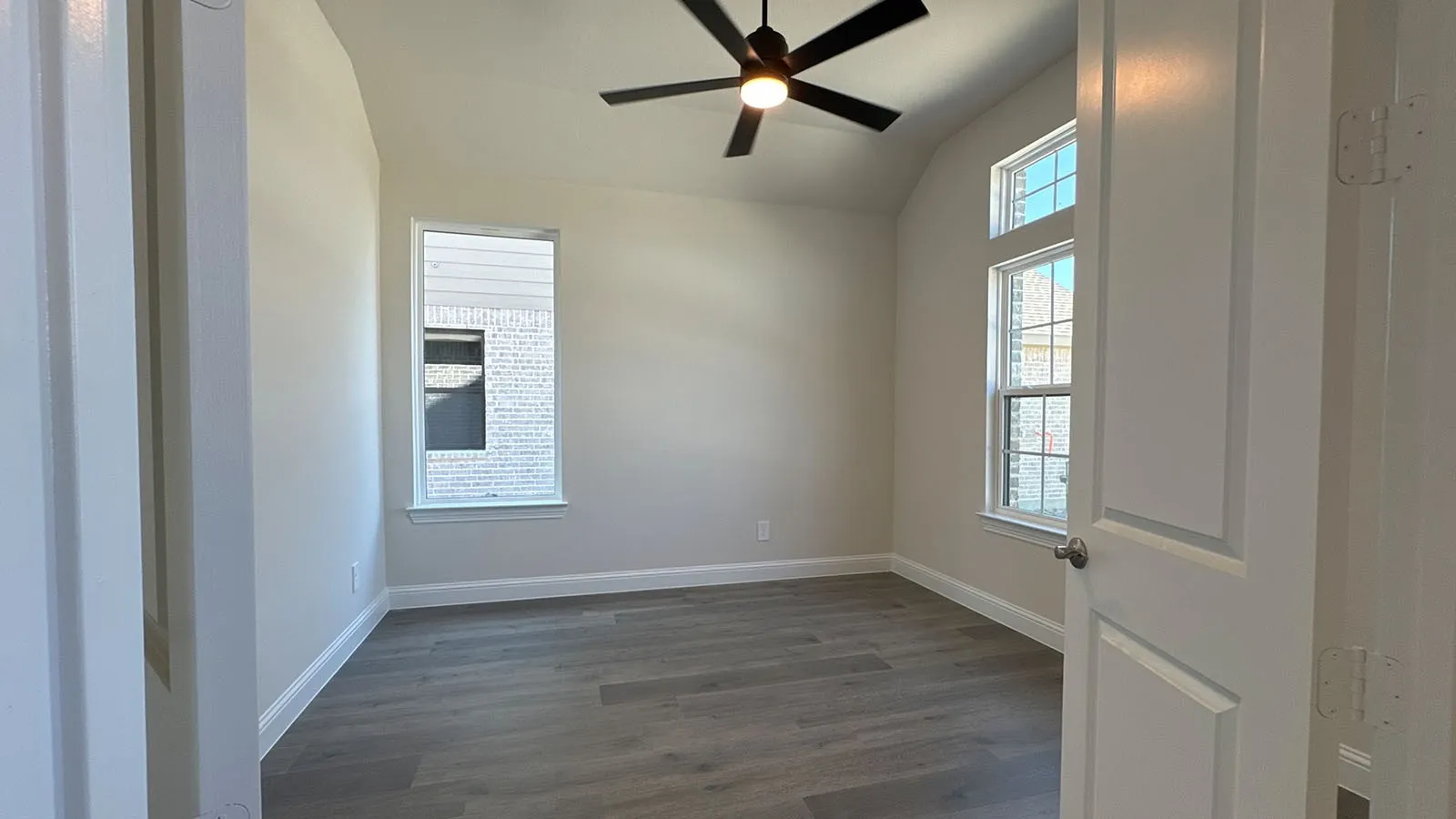 Vaulted ceiling with a black ceiling fan, wood-finish flooring, and multiple windows providing natural illumination