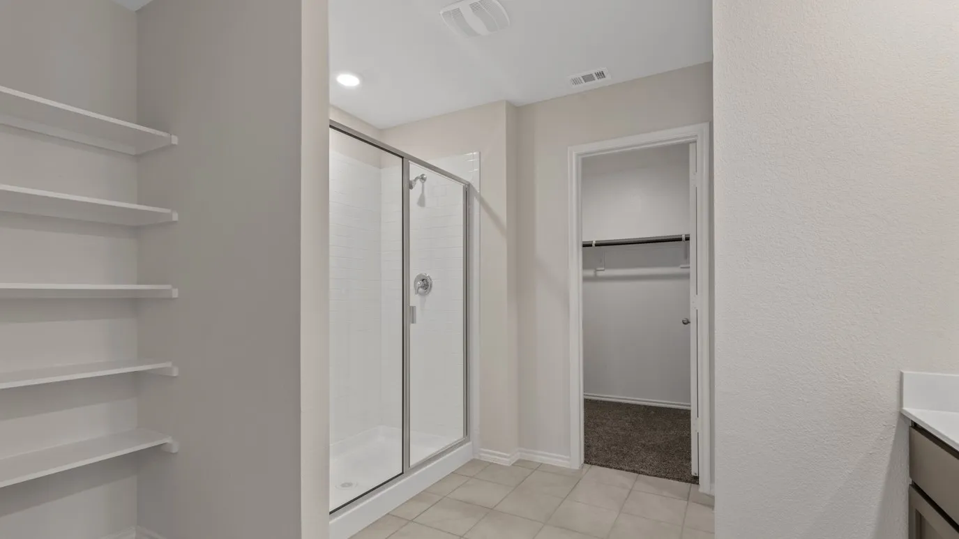 Built-in shelving, glass-enclosed shower with tile surround, and an adjacent walk-in closet with carpet flooring