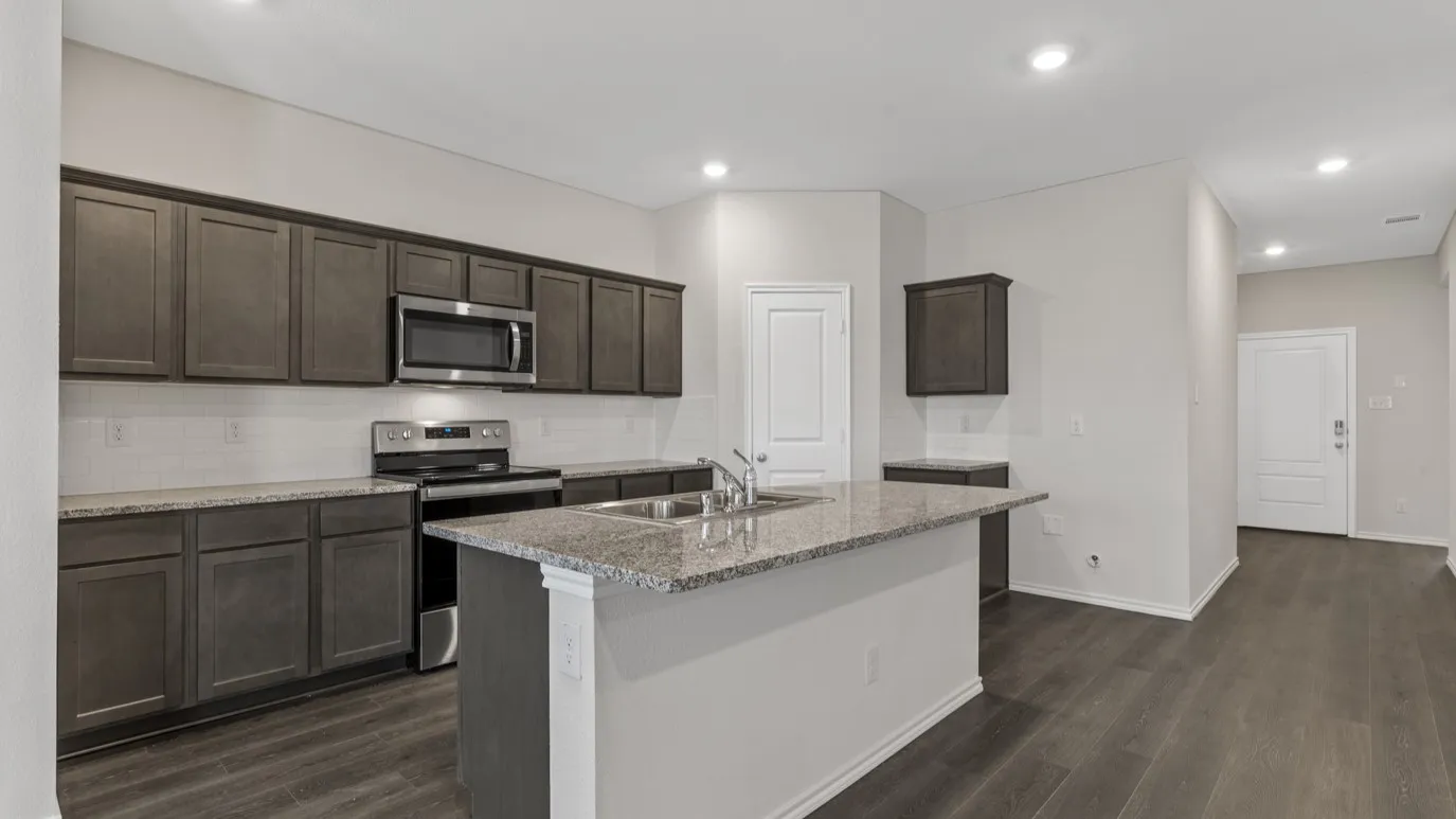 Kitchen featuring dark wood-finish cabinetry, granite countertops, stainless steel appliances, and a central island with a sink