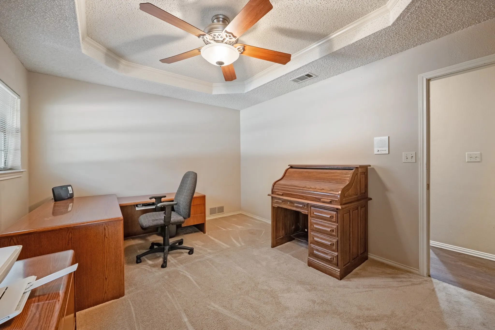 Tray ceiling with crown molding, ceiling fan, neutral wall paint, and carpeting