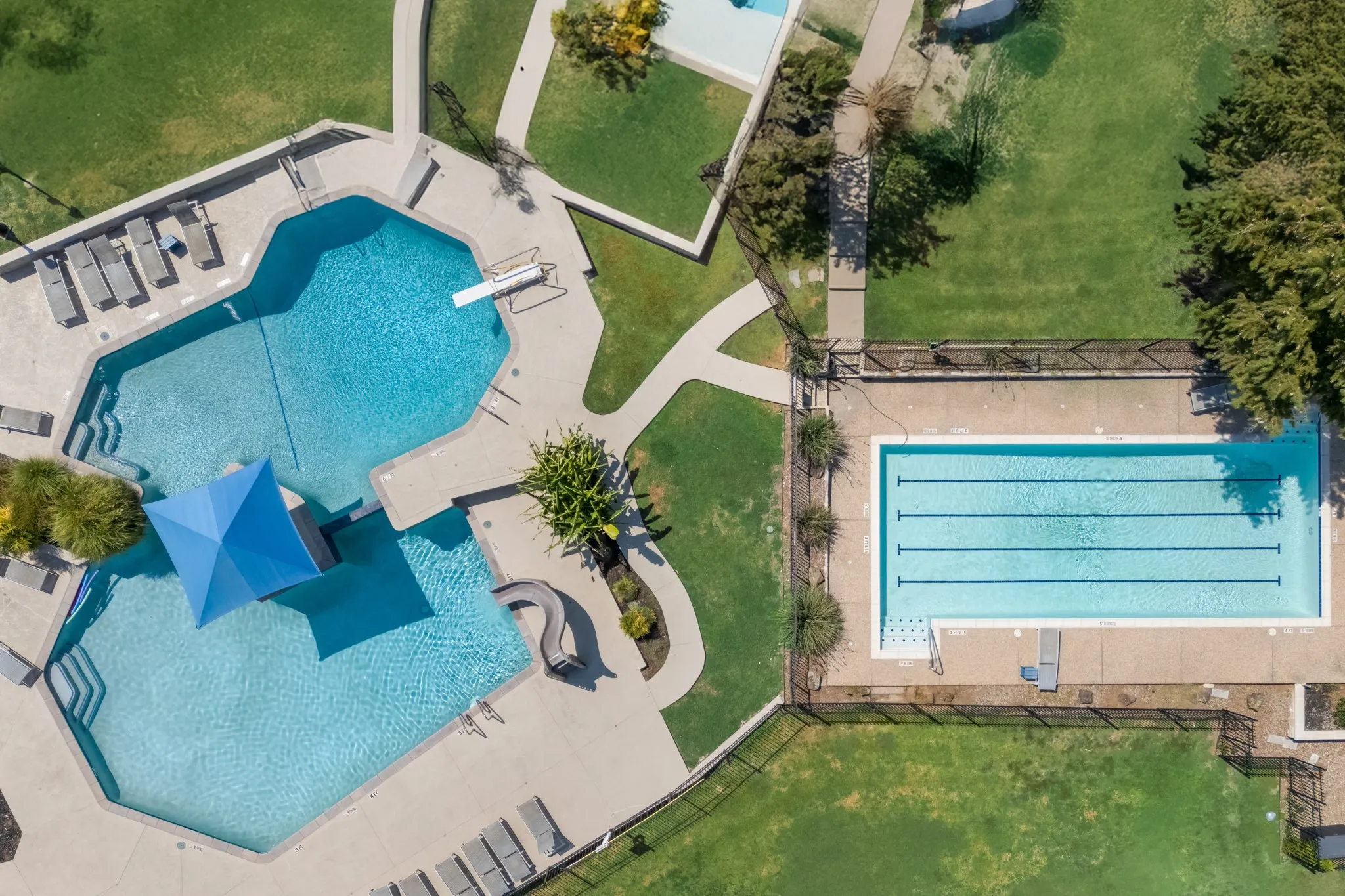 Expansive outdoor area featuring two distinct pools, concrete pool decks, a diving board, and a water slide
