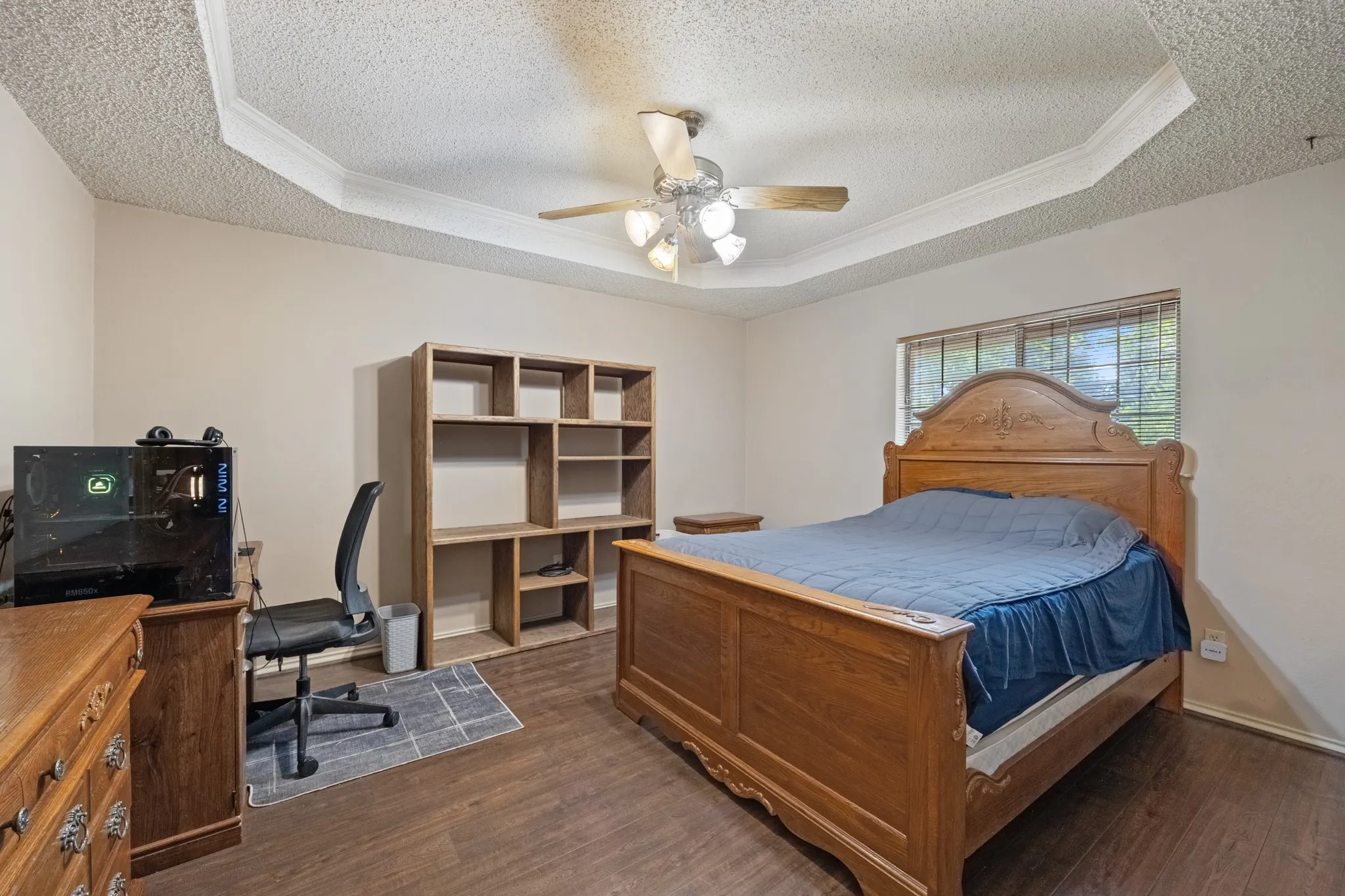 Tray ceiling with crown molding, ceiling fan, wood-finish flooring, built-in shelving, and window with exterior view
