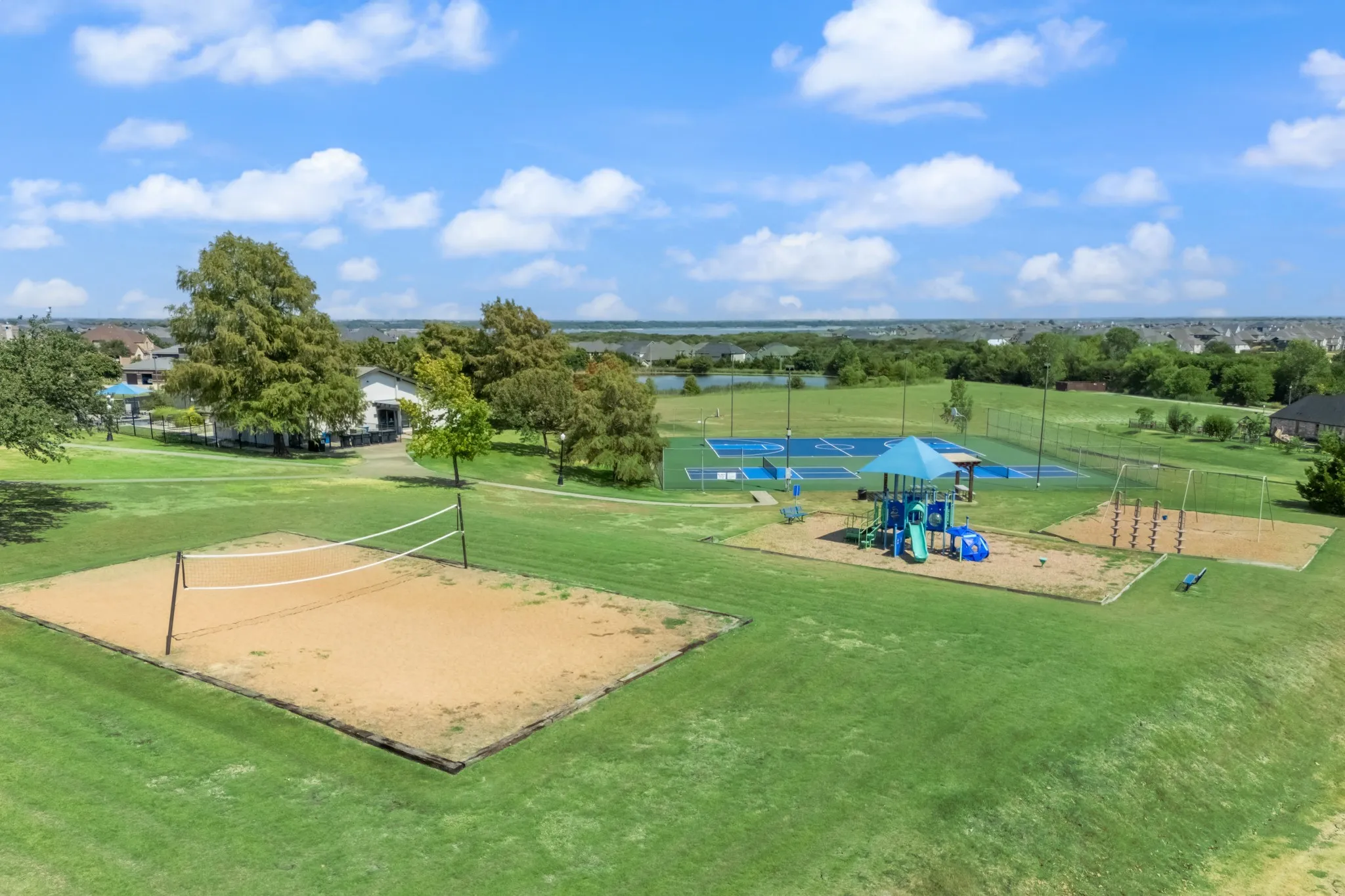 Expansive green space featuring a sand volleyball court, a playground structure, and multiple tennis/pickleball courts