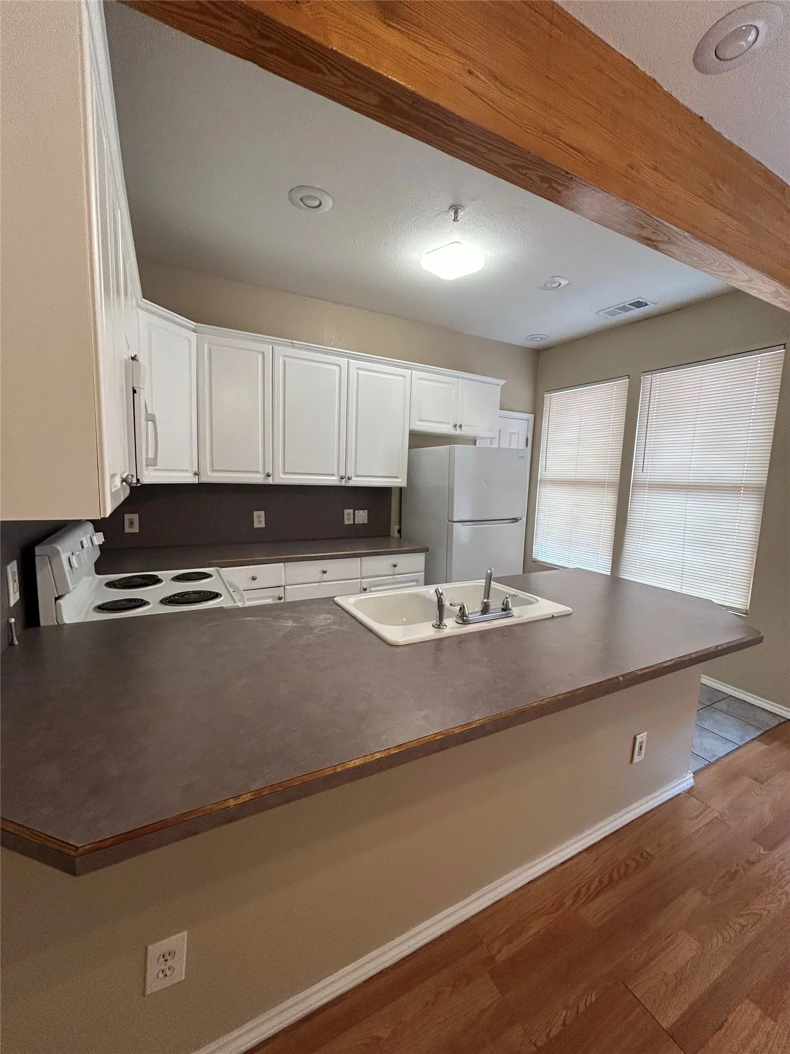 Kitchen featuring white cabinetry, a built-in sink, wood-finish flooring, an exposed wood beam, and recessed lighting