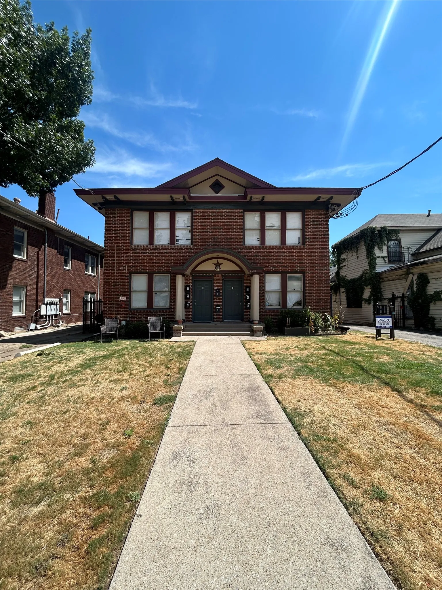 Brick facade with multiple windows and a central concrete walkway leading to dual entrances