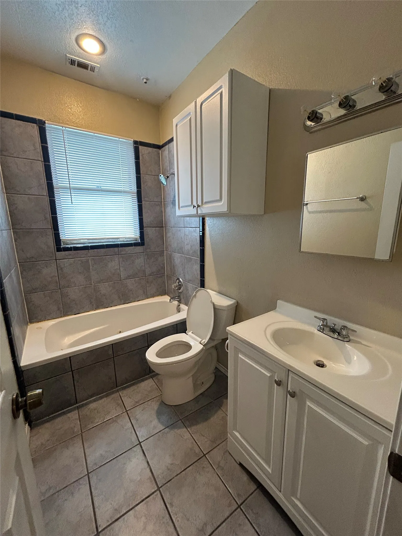 Bathroom featuring a tiled tub surround, white vanity with integrated sink, and upper white cabinetry