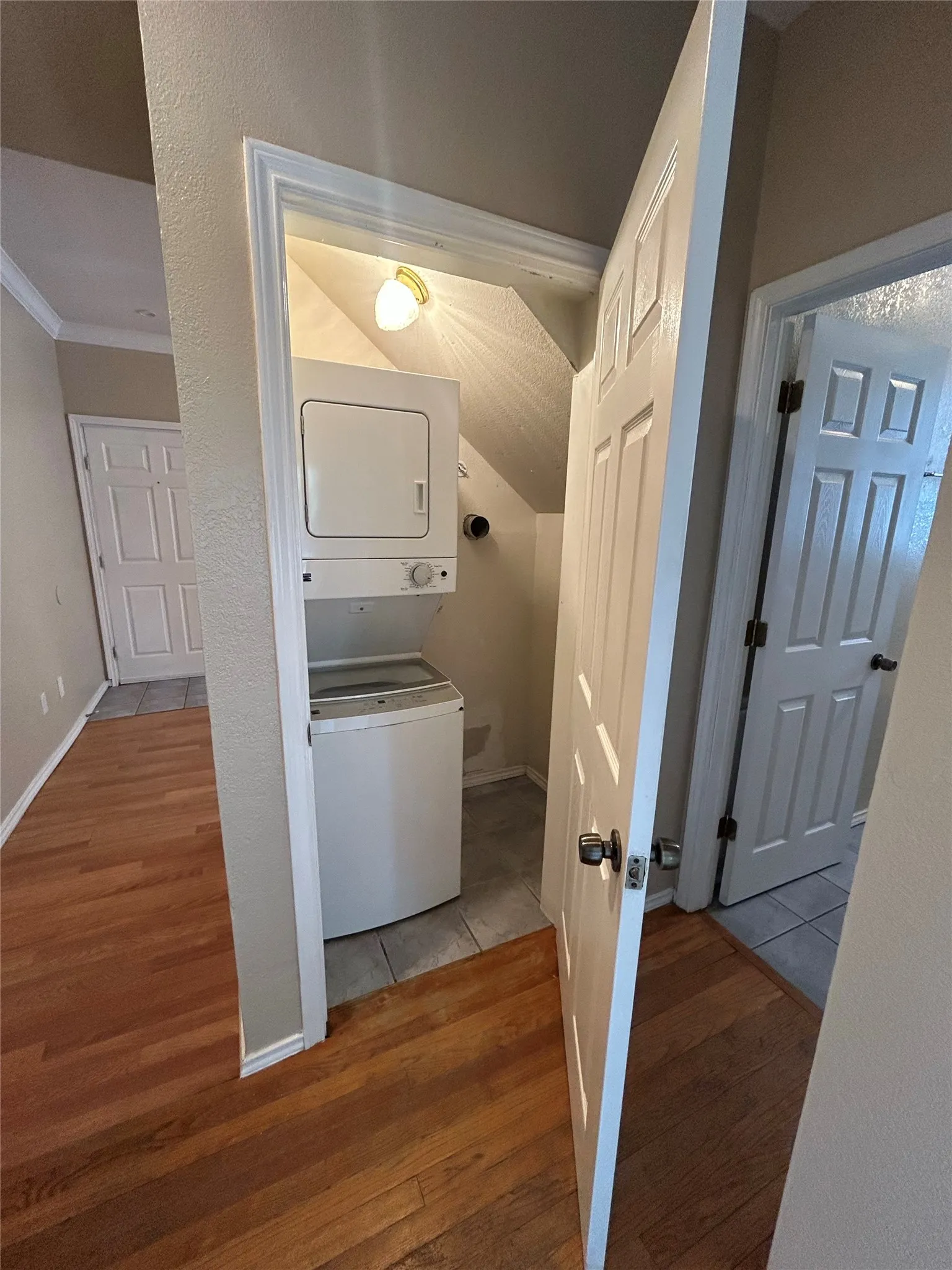 Wood-finish flooring throughout, with a tiled laundry area featuring a stackable washer and dryer unit, and a surface-mounted light fixture