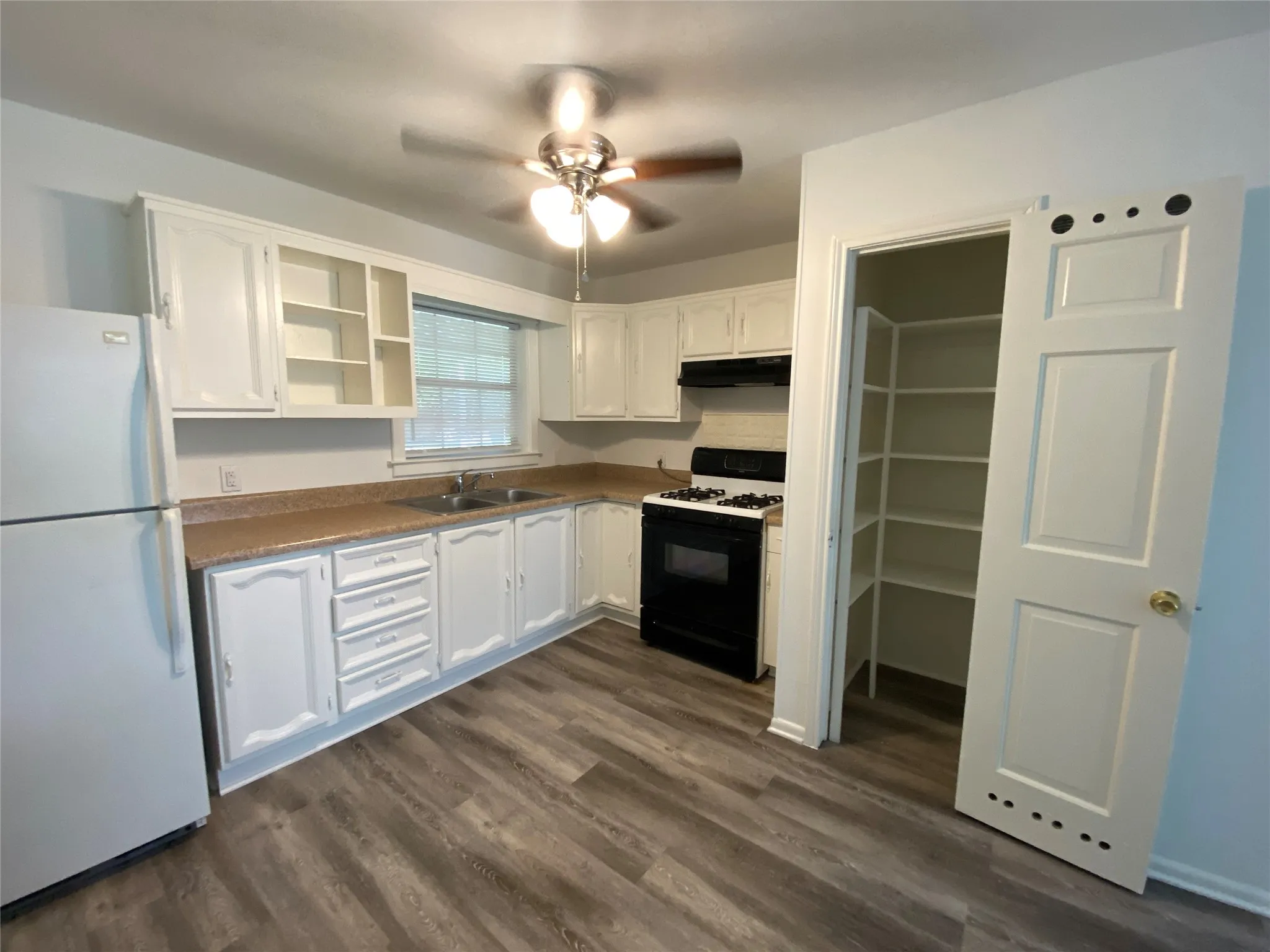 Kitchen featuring wood-finish flooring, white cabinetry, a double basin sink, and a built-in pantry with shelving