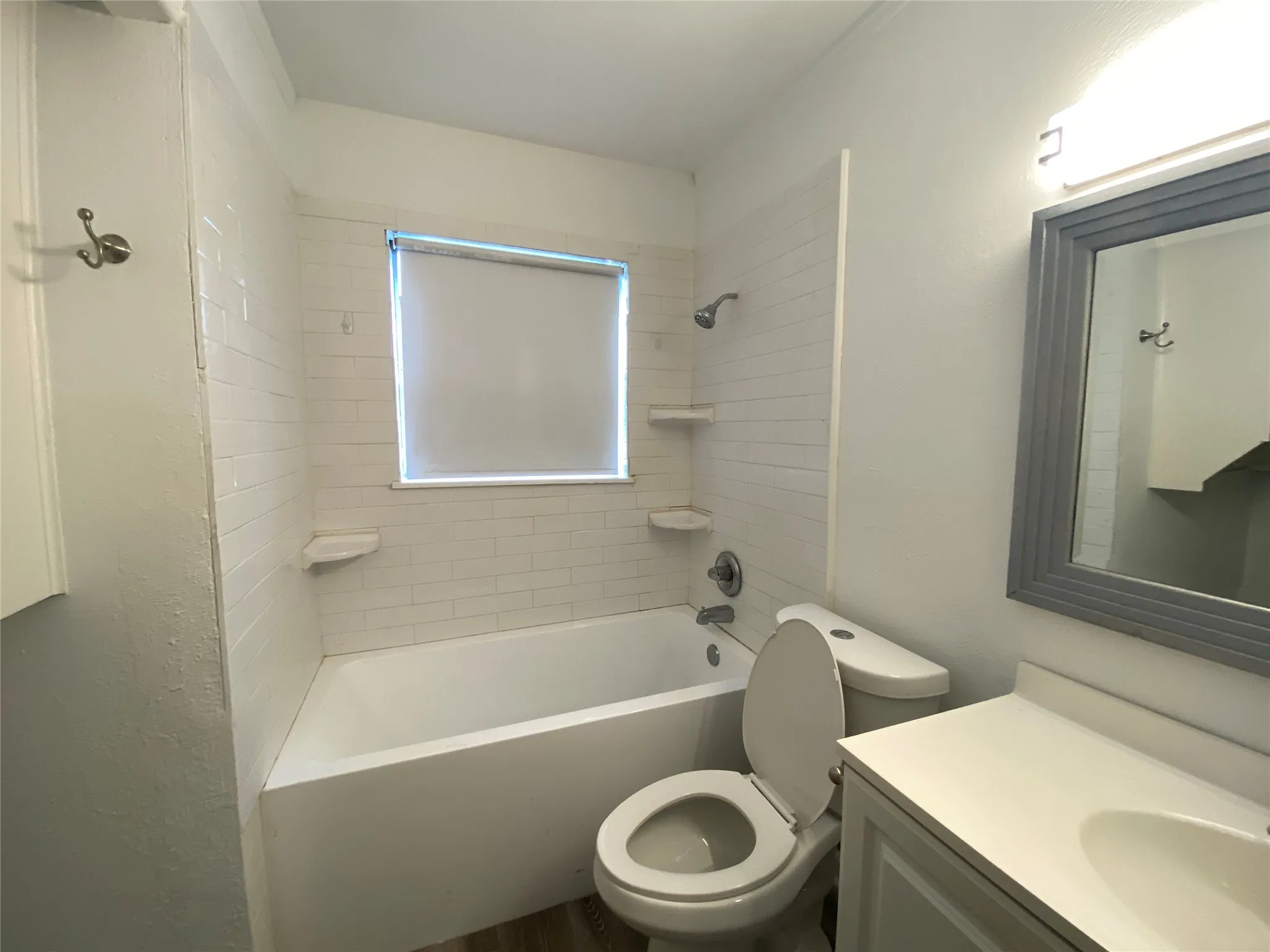 White subway tile tub surround, built-in shelving, window with roller shade, and a vanity with an integrated sink