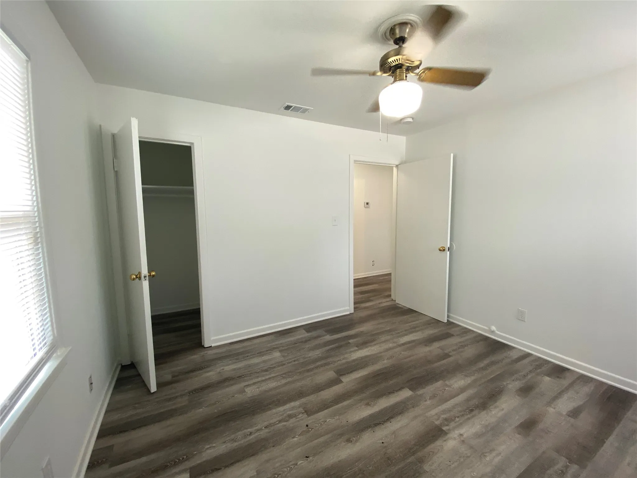 Wood-finish flooring, ceiling fan with light fixture, white walls, built-in closet with shelving, and window with blinds