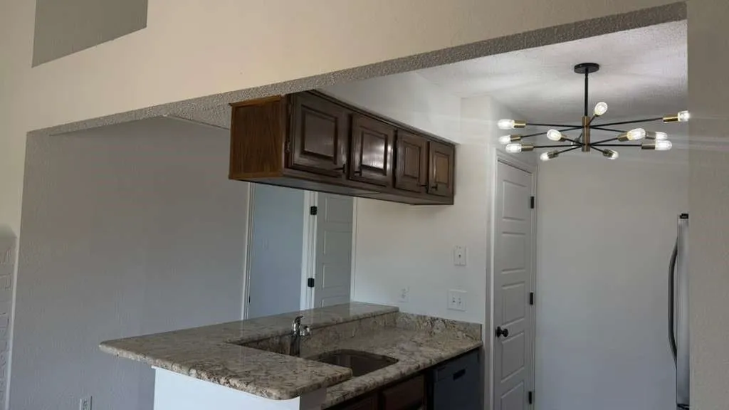 Granite-finish countertops, undermount sink, dark wood-finish cabinetry, and a contemporary sputnik chandelier
