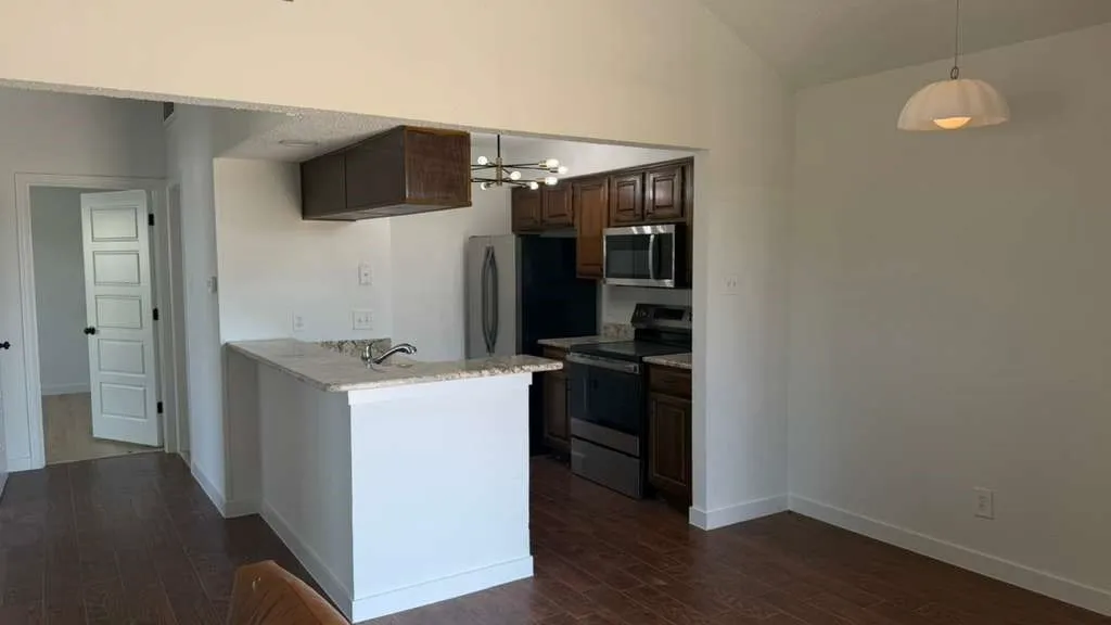 Kitchen featuring dark wood cabinetry, stainless steel appliances, a breakfast bar with stone countertops, and wood-finish flooring