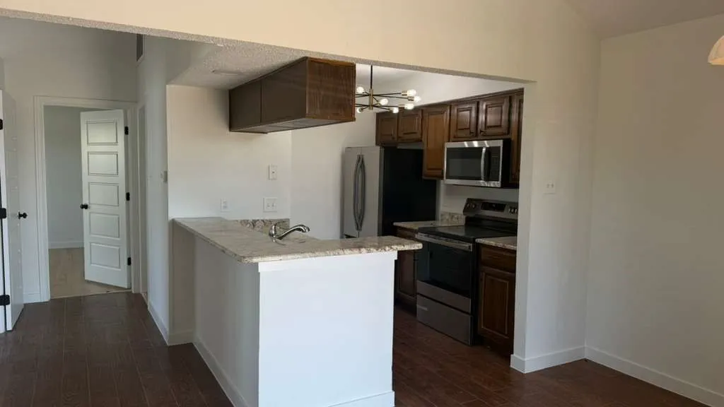 Kitchen featuring dark wood cabinetry, stainless steel appliances, a breakfast bar with stone countertops, and wood-finish flooring