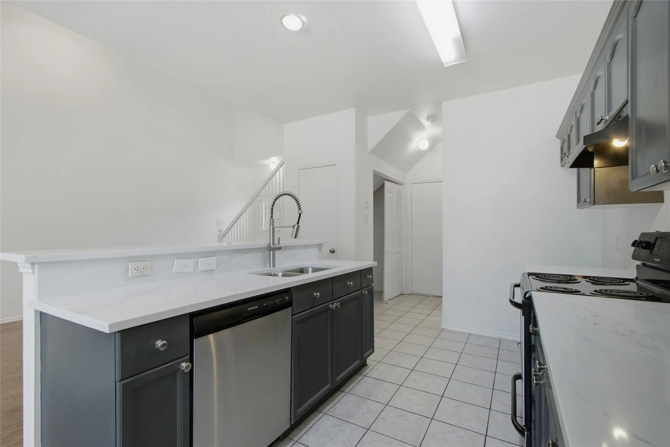 Kitchen featuring white countertops, dark gray cabinetry, a stainless steel dishwasher, a chrome pull-down faucet, and white tile flooring