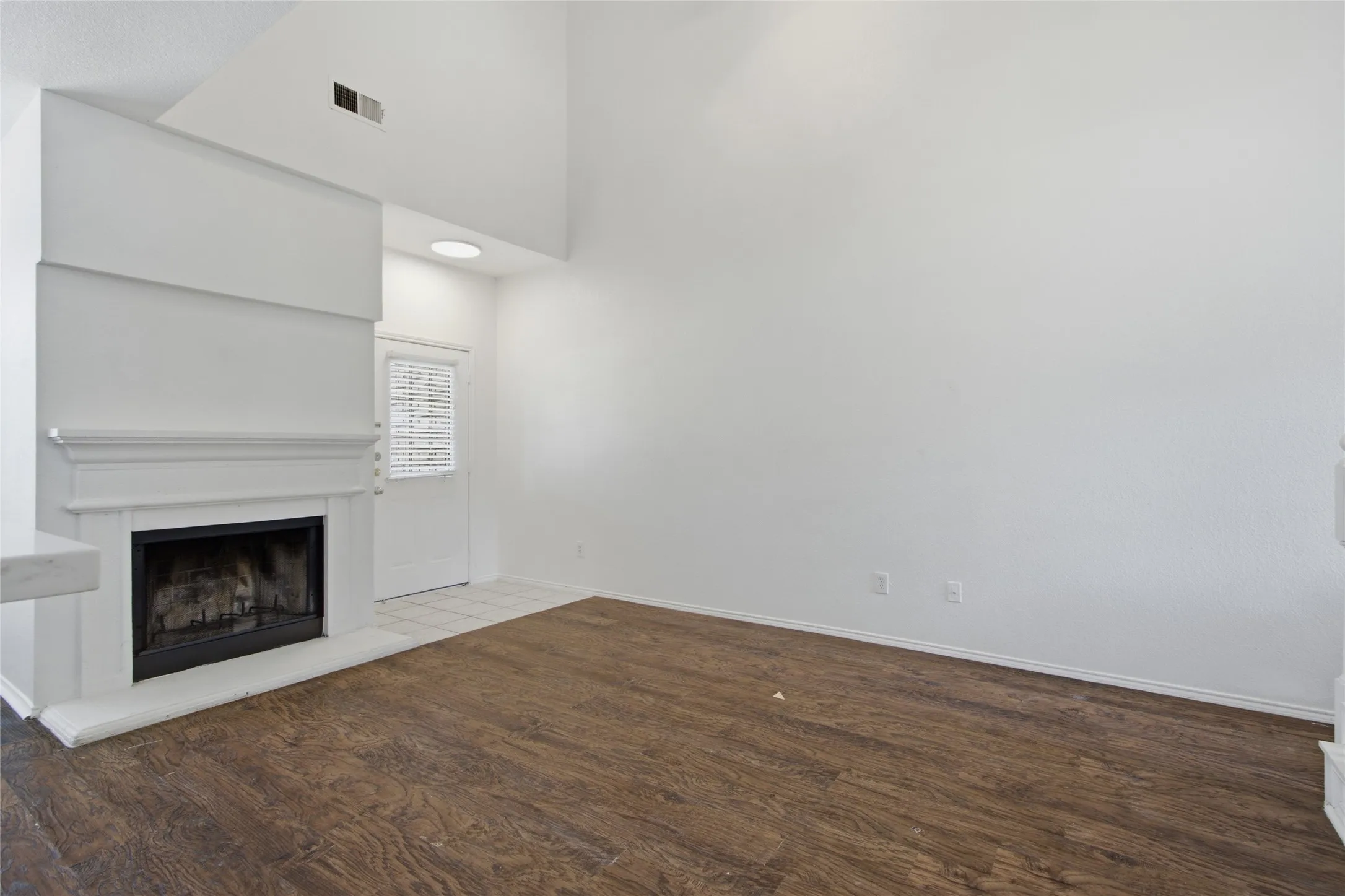 Living area featuring vaulted ceilings, a prominent fireplace with a white mantel, wood-finish flooring, and white interior walls