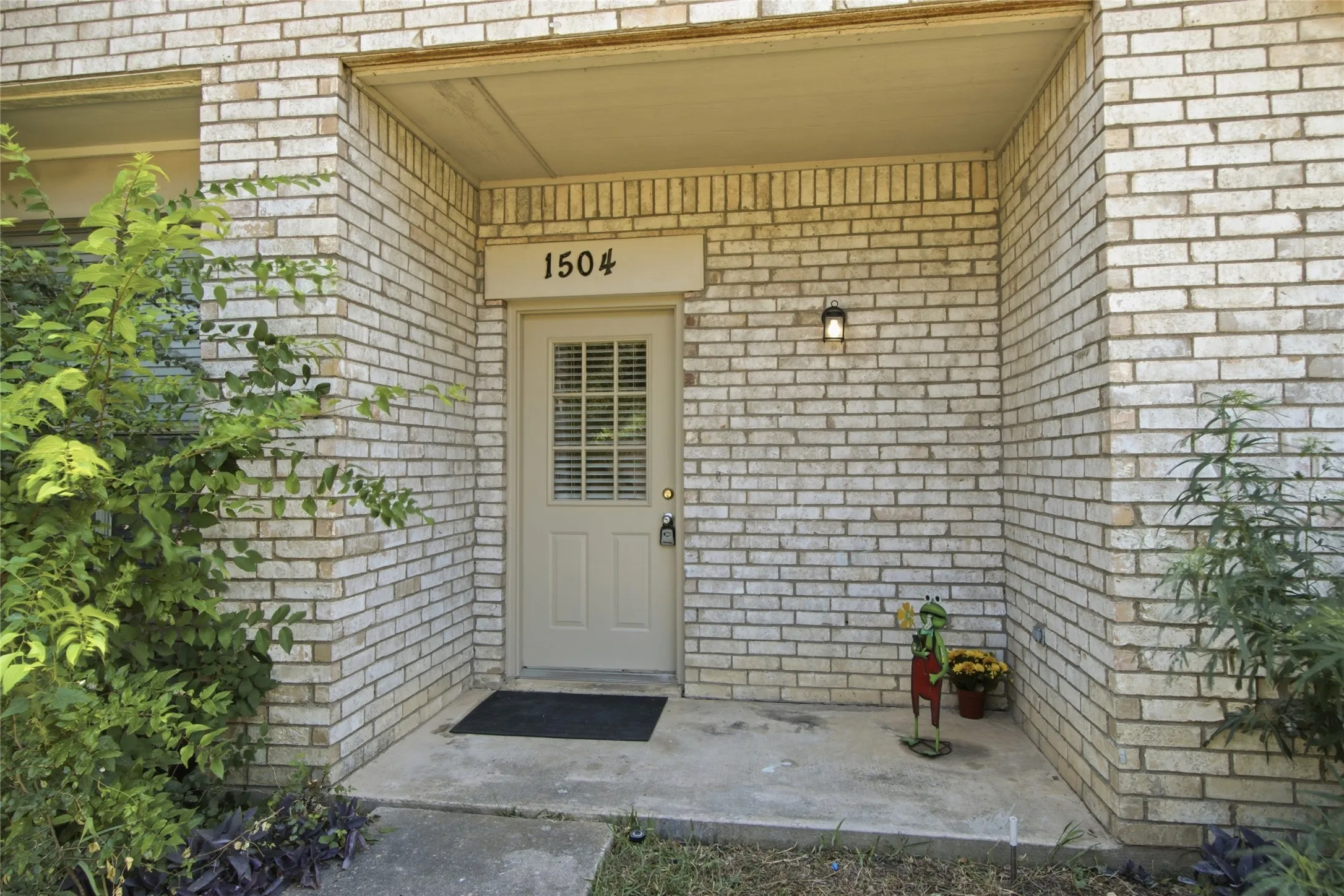 Brick exterior featuring an entry door with glass paneling, overhead lighting, and concrete porch