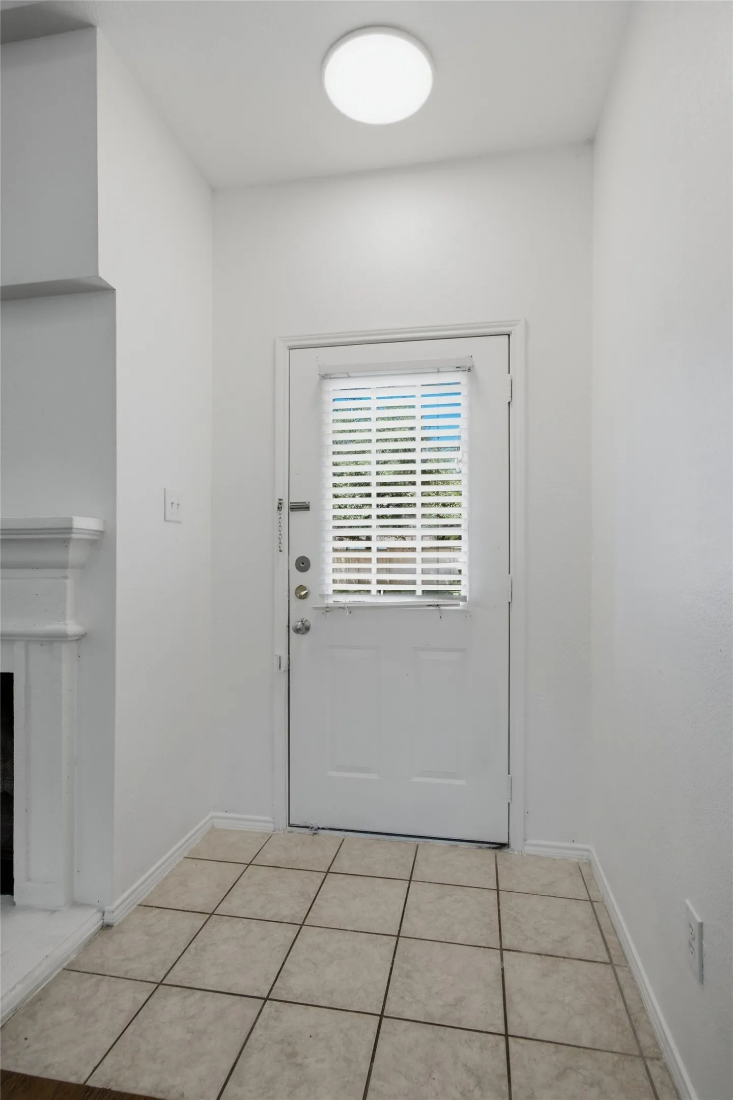 Entryway featuring light-toned tile flooring, a white door with an integrated louvered window, and a flush-mount ceiling light fixture