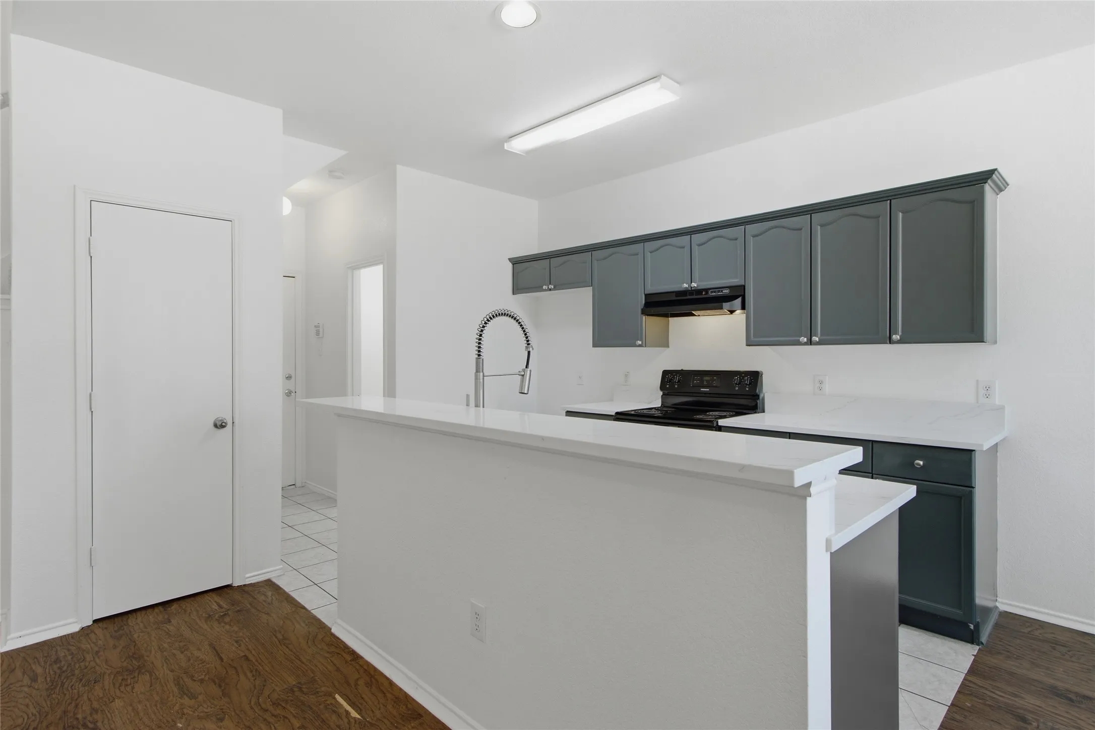 Kitchen featuring dark gray cabinetry, white countertops, a black electric range, and a breakfast bar with a gooseneck faucet