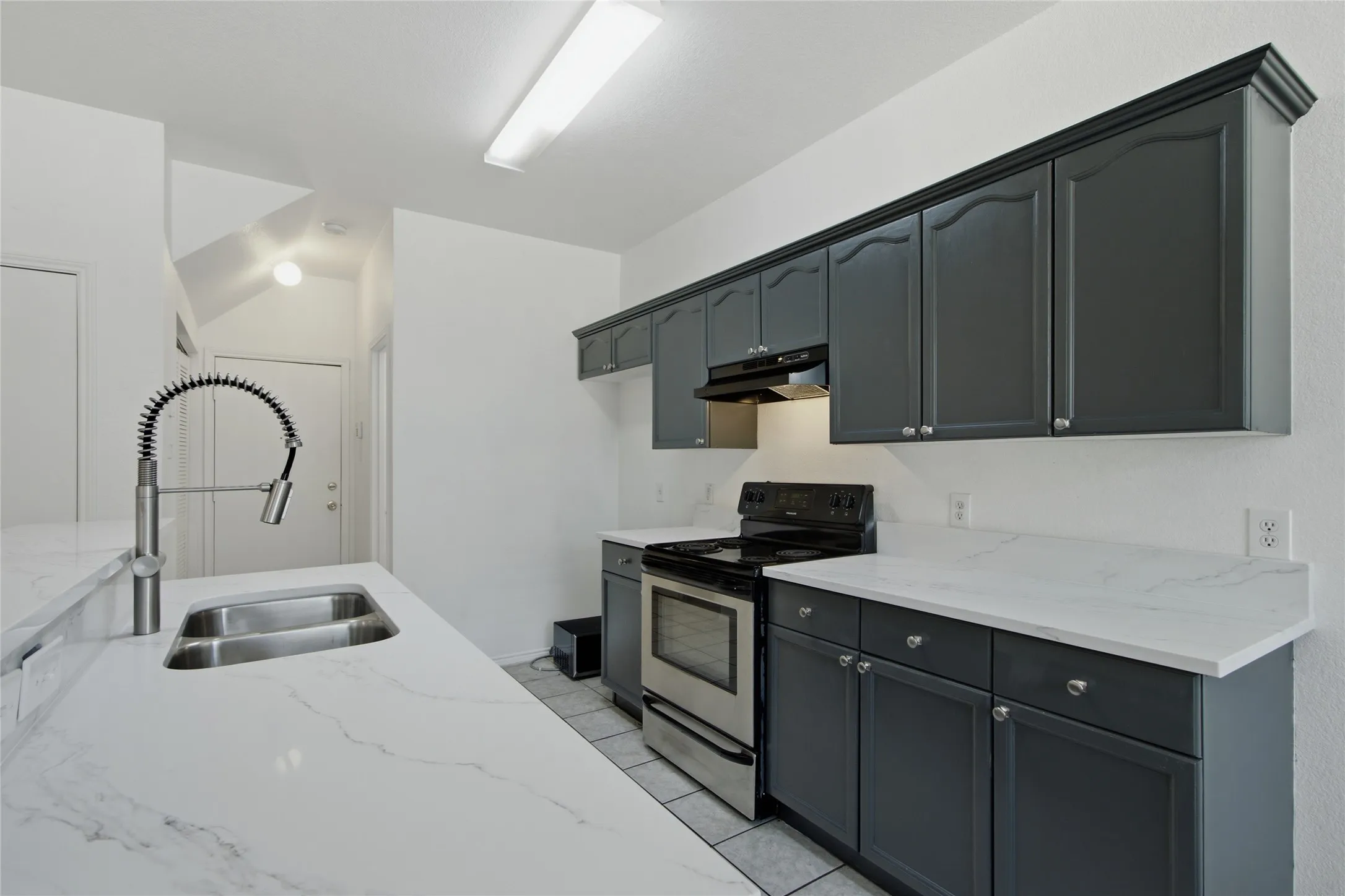 Kitchen featuring grey cabinetry with silver hardware, white countertops, dual basin stainless steel sink with a pull-down faucet, and a stainless steel oven range with an overhead vent
