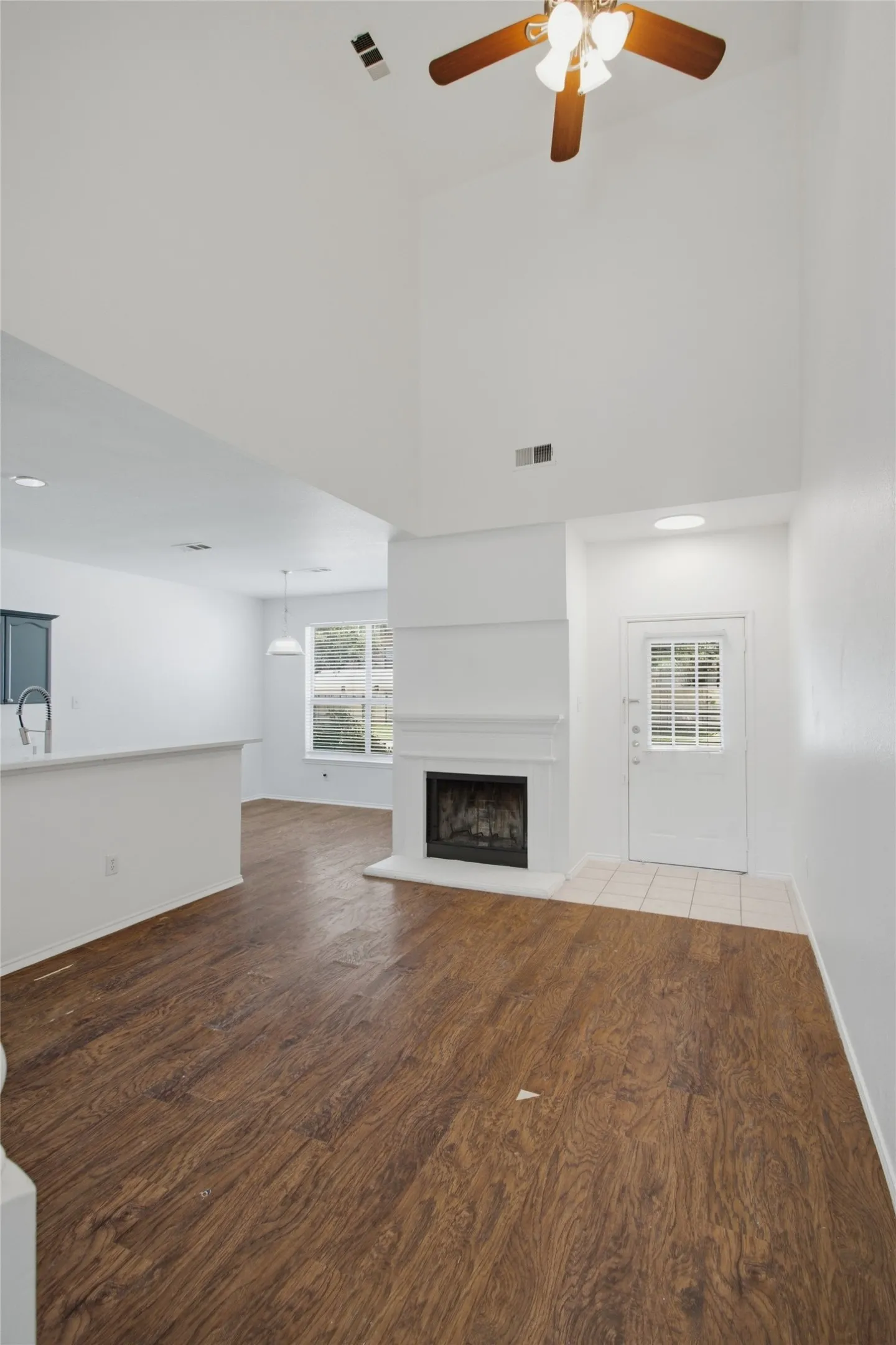 Living area with high ceilings, wood-finish flooring, and a fireplace with a white mantel