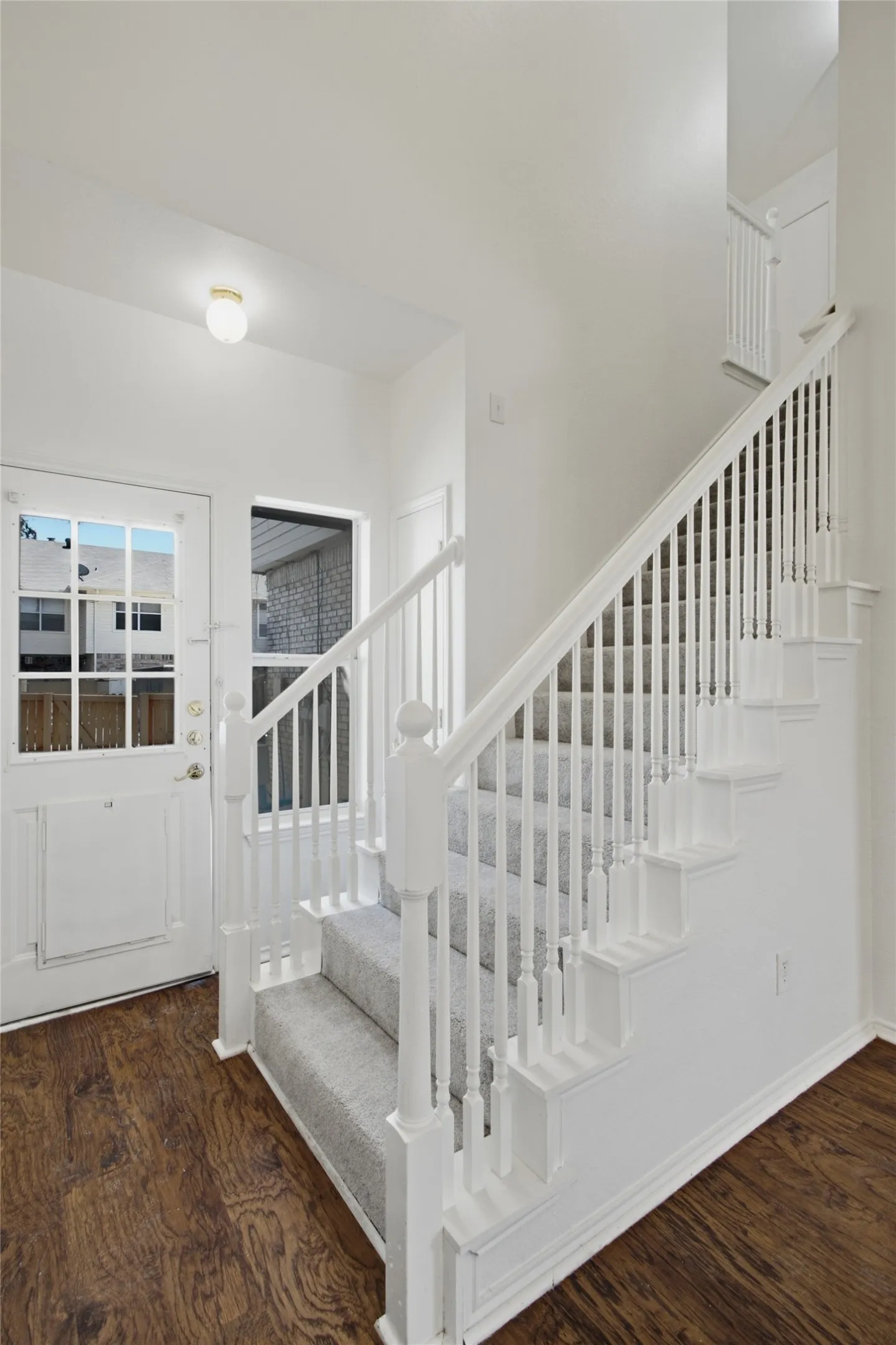Staircase with white balusters and carpeted treads, wood-finish flooring, white entry door with glass panels, and a window