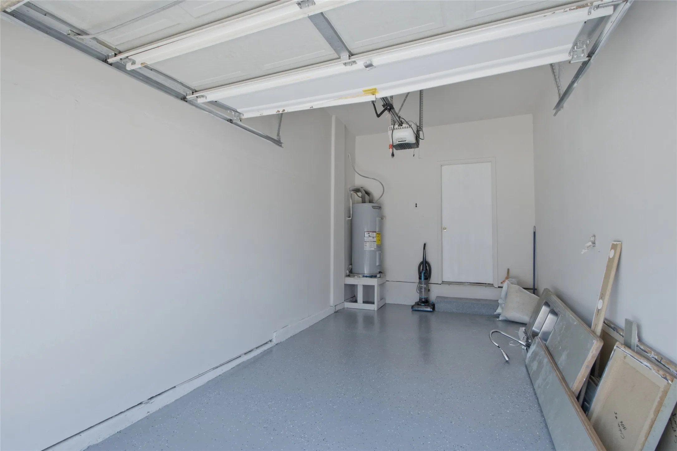 Garage featuring a roll-up door, epoxy-coated concrete flooring, a water heater, and a side entry door