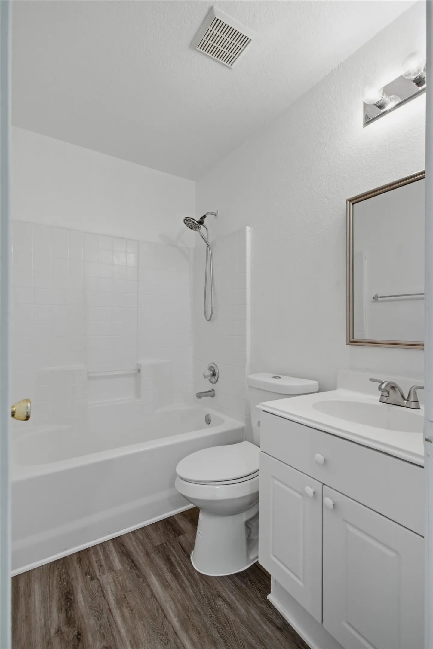 Bathroom featuring a white bathtub with tile surround, a white toilet, and a white vanity with an integrated sink and base cabinetry